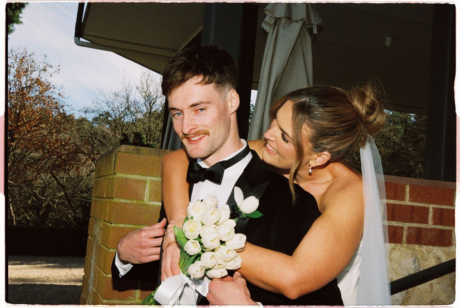 Happy bride and groom embracing outdoors, bride holding white tulip bouquet.