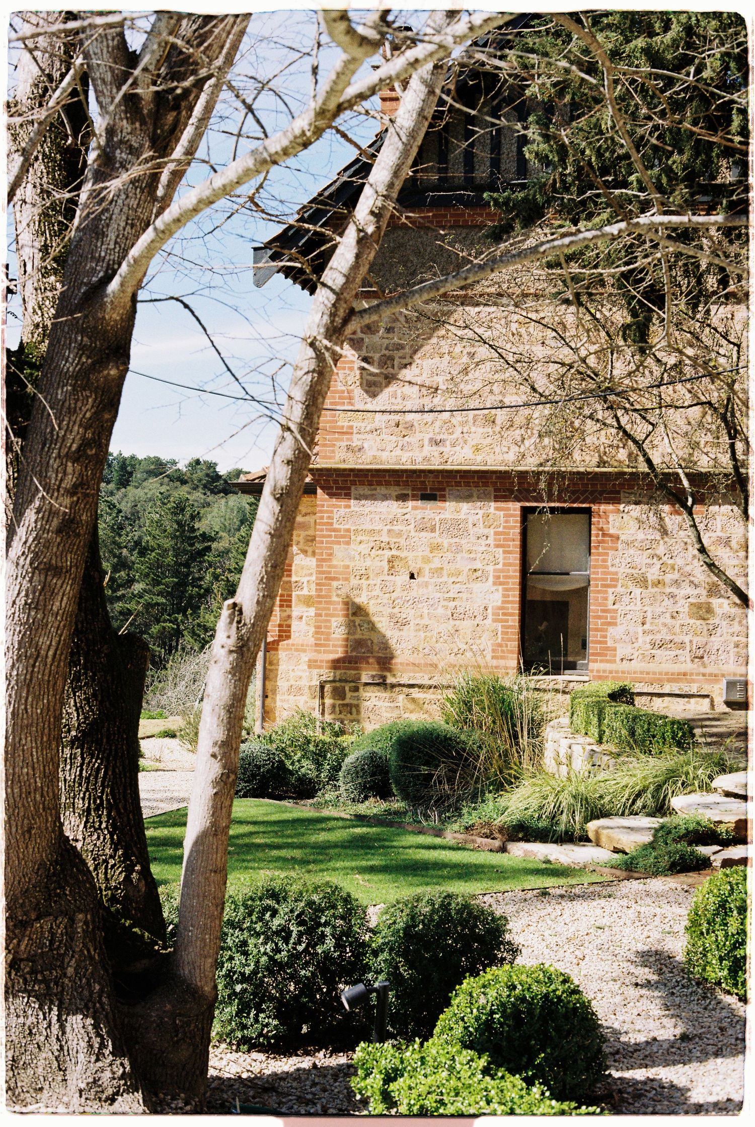 Stone brick wedding venue with manicured hedges and trees casting shadows on a sunny day.