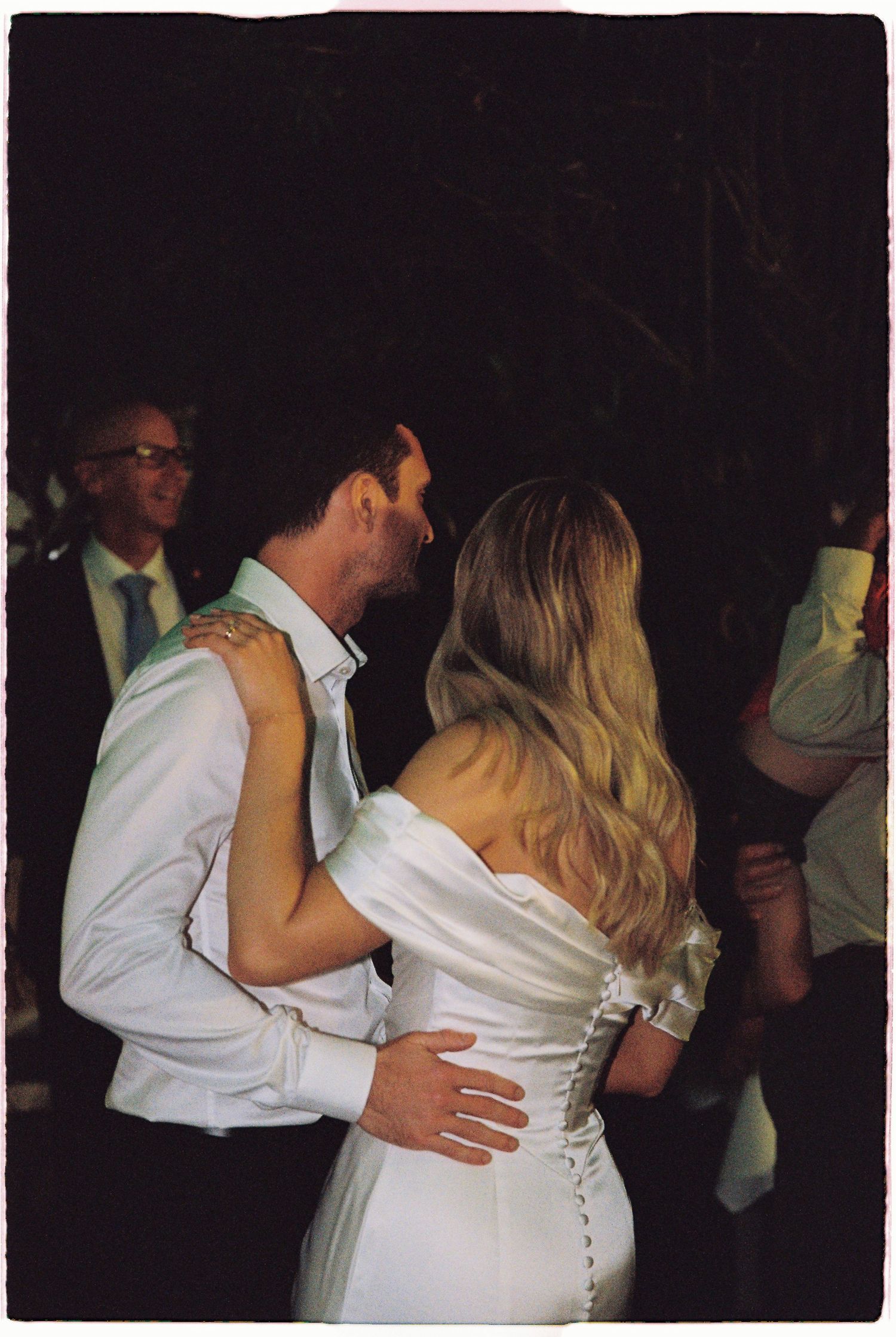 A bride in a white off-shoulder gown shares a first dance kiss with her groom in a white shirt at their wedding.