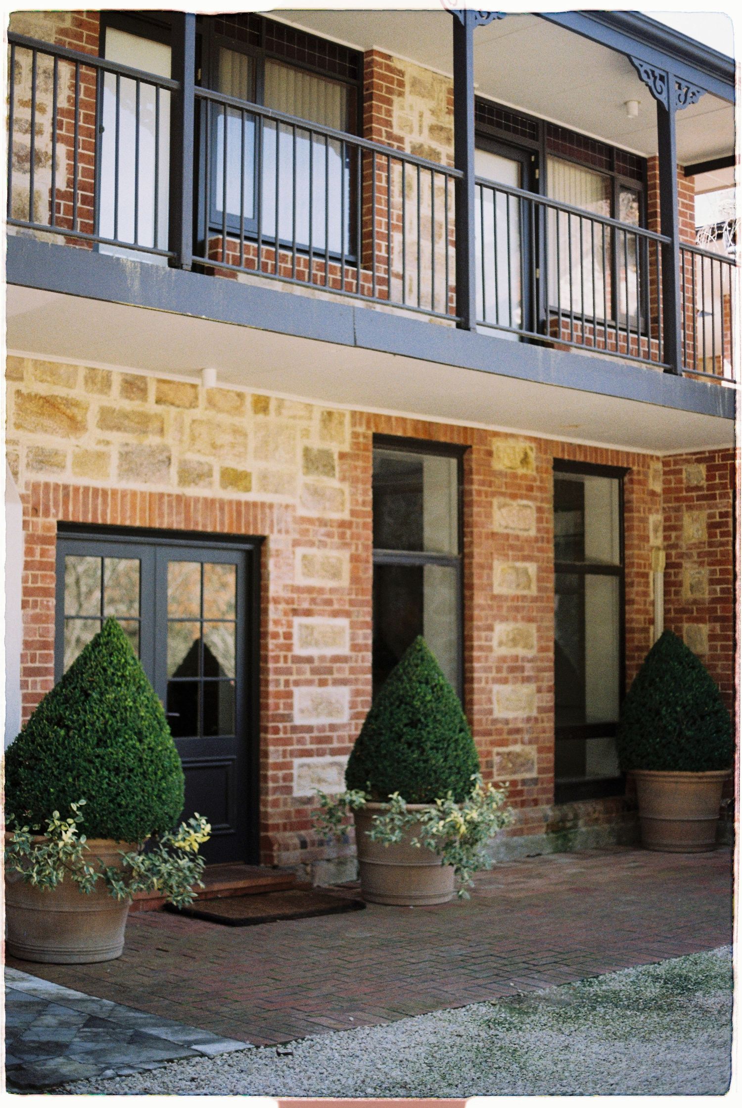 Stone and brick building exterior with black balcony railing and manicured topiary in pots.