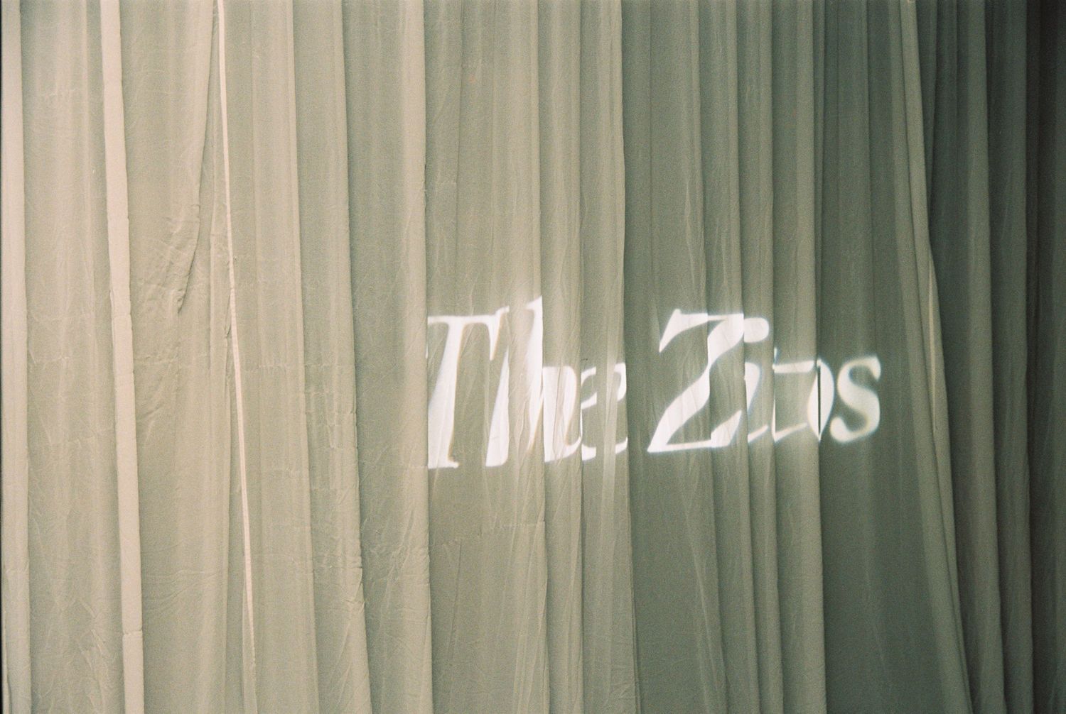 Sheer white curtains display projected text reading The Zins at a wedding venue.