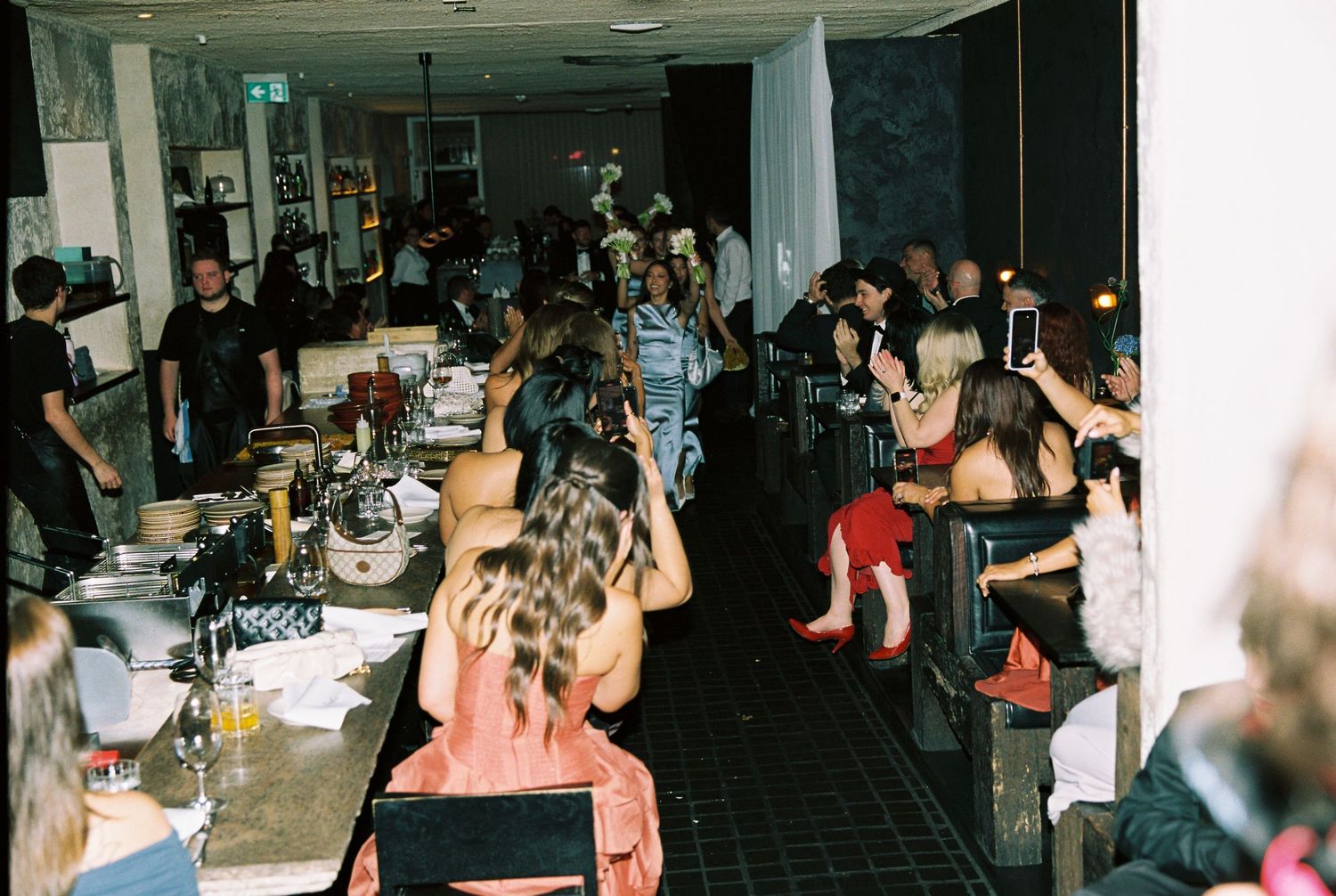 Guests seated and mingling at a long table during a vibrant indoor wedding reception.