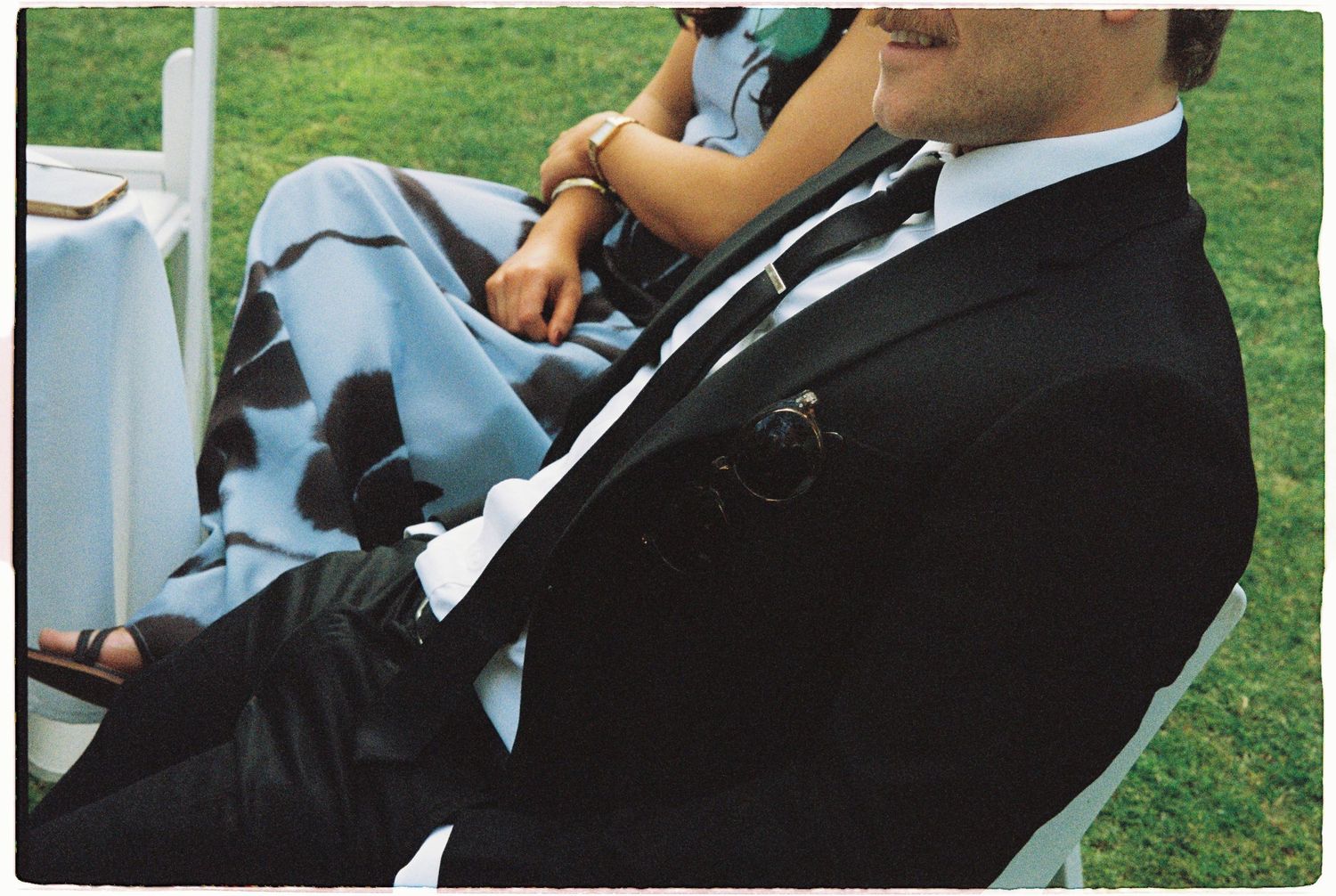 Wedding guest in black suit seated beside woman in floral dress at ceremony.