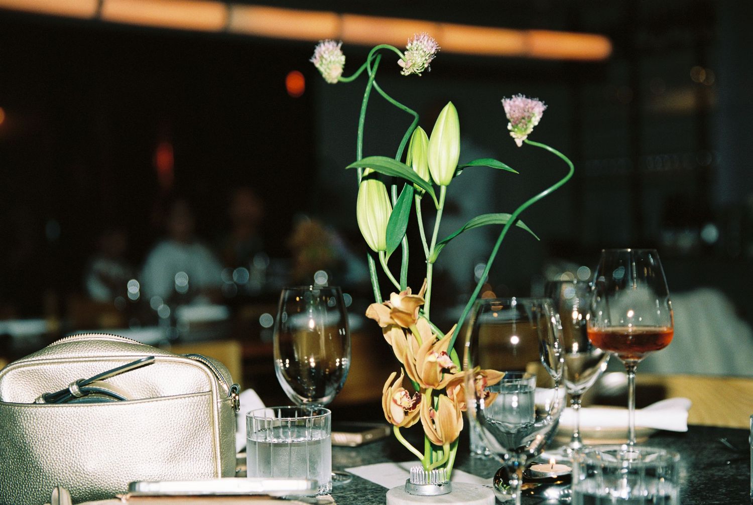 Elegant floral centerpiece with orchids and tall stems surrounded by wine glasses at a formal dinner.