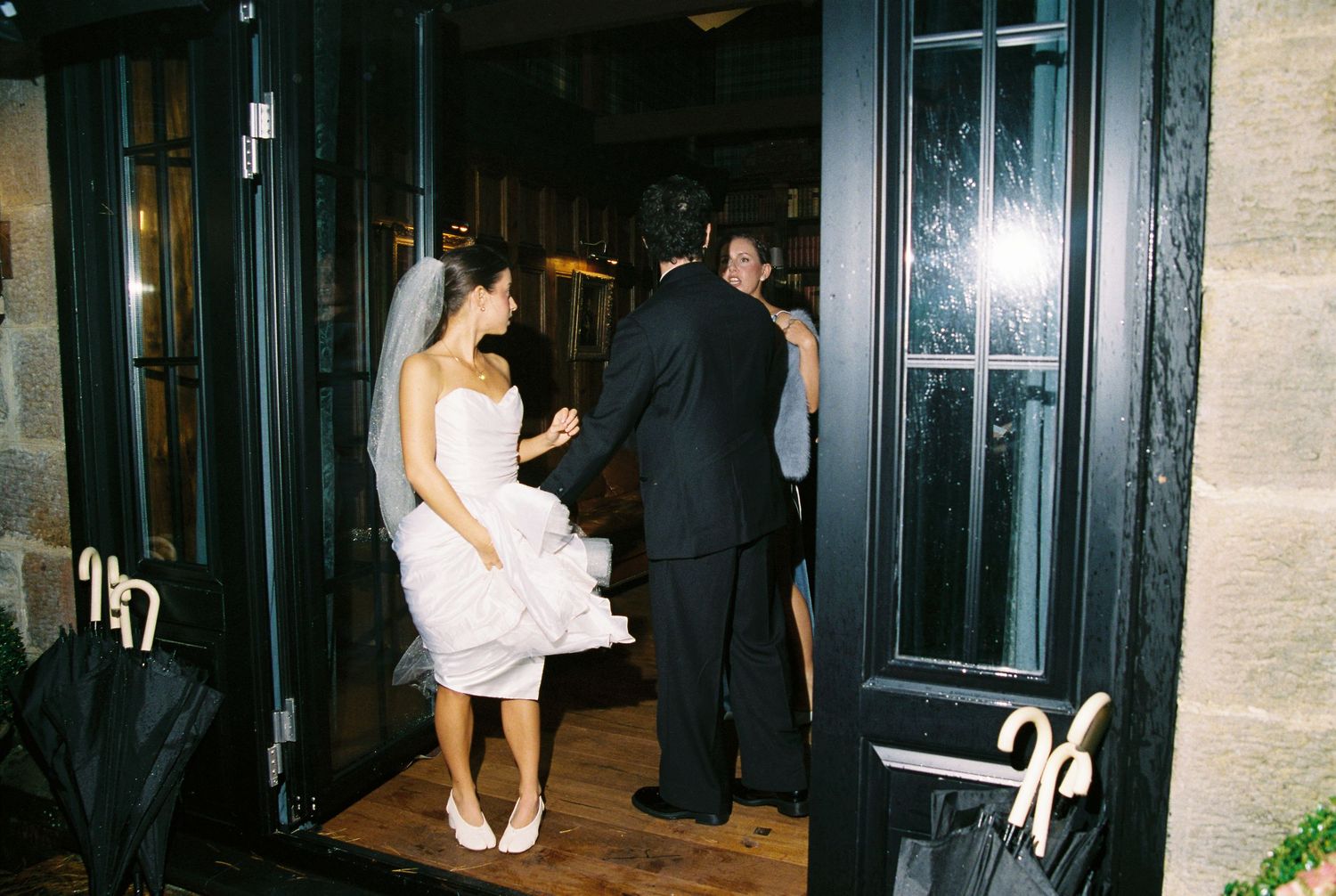 Bride in white dress and groom in black suit entering venue through dark wooden doors on wedding day.