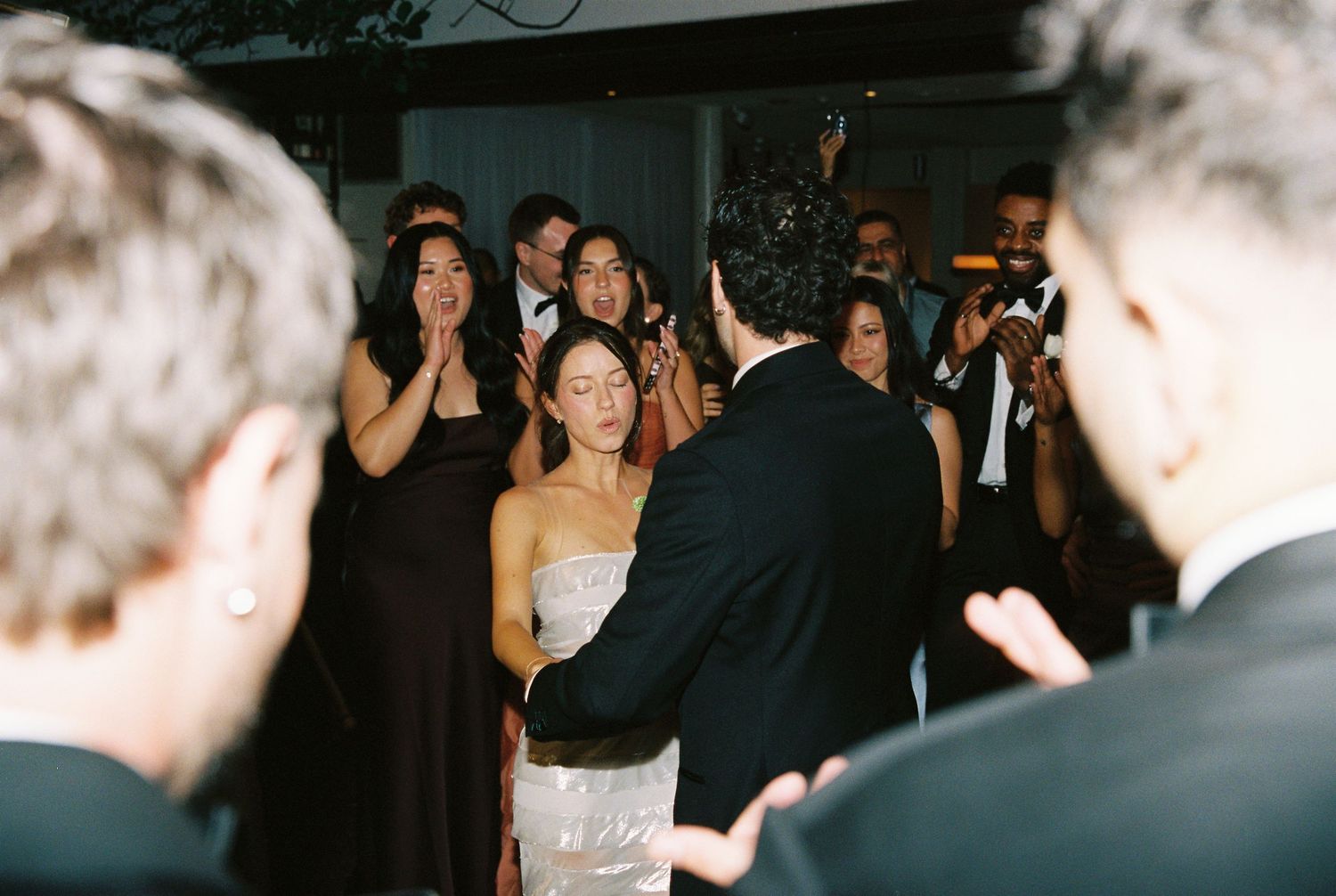 Bride and groom share an emotional first dance surrounded by applauding guests at their wedding reception.