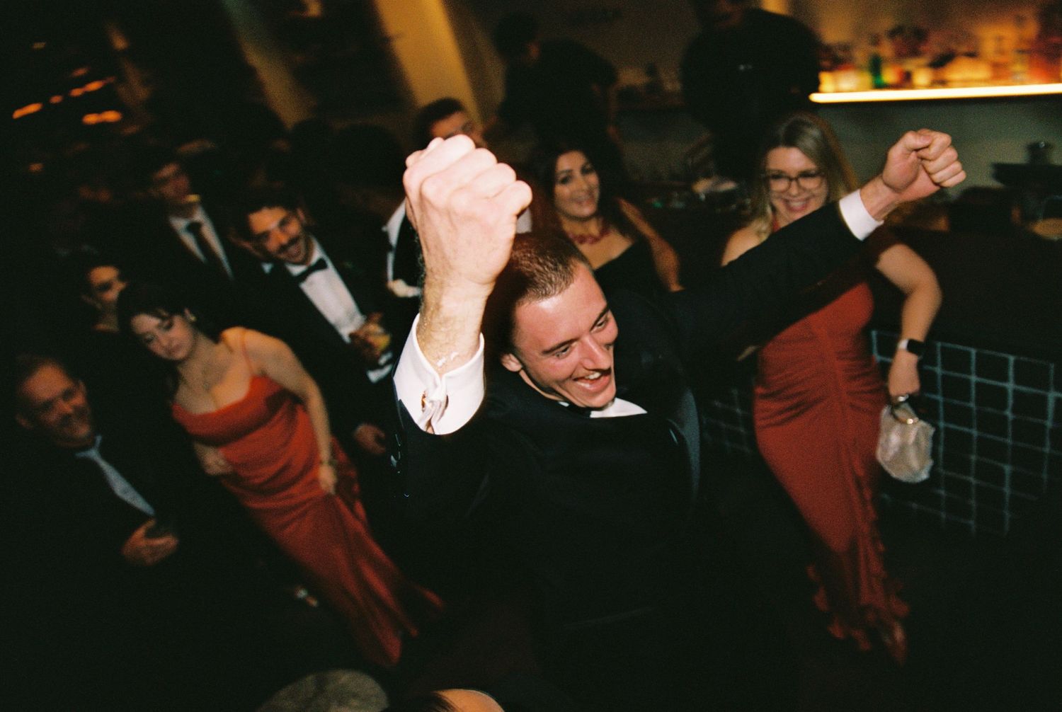 Energetic wedding guest dances joyfully with raised fists on the dance floor at evening reception.