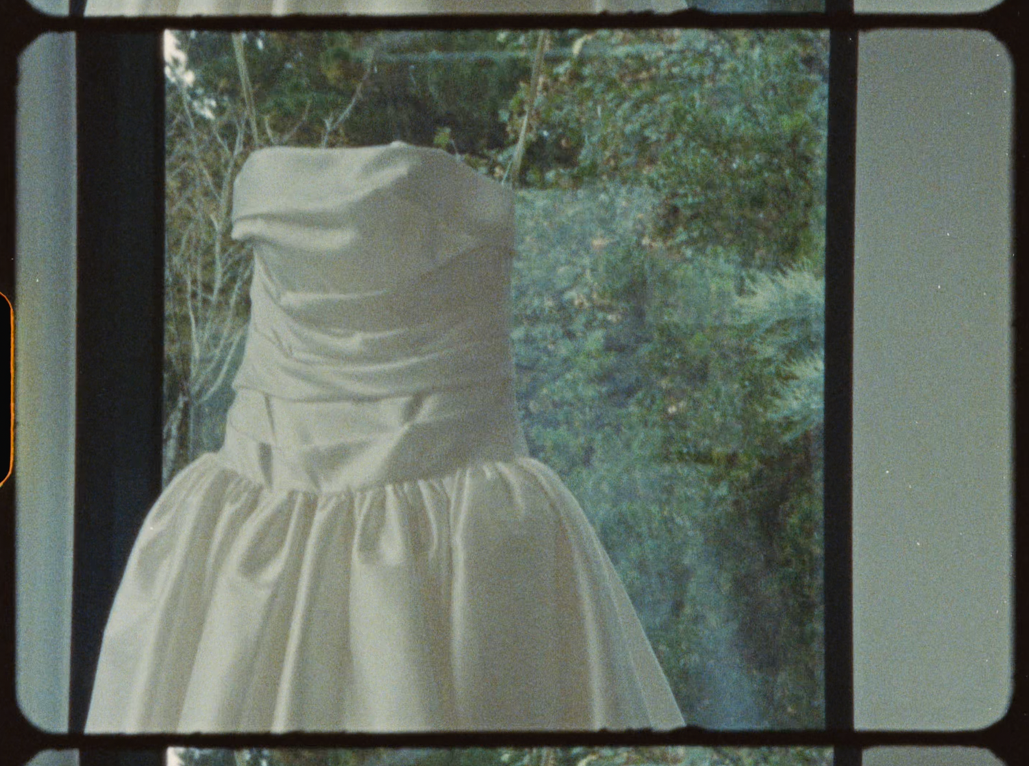 Elegant strapless white wedding dress displayed against a lush green garden backdrop.