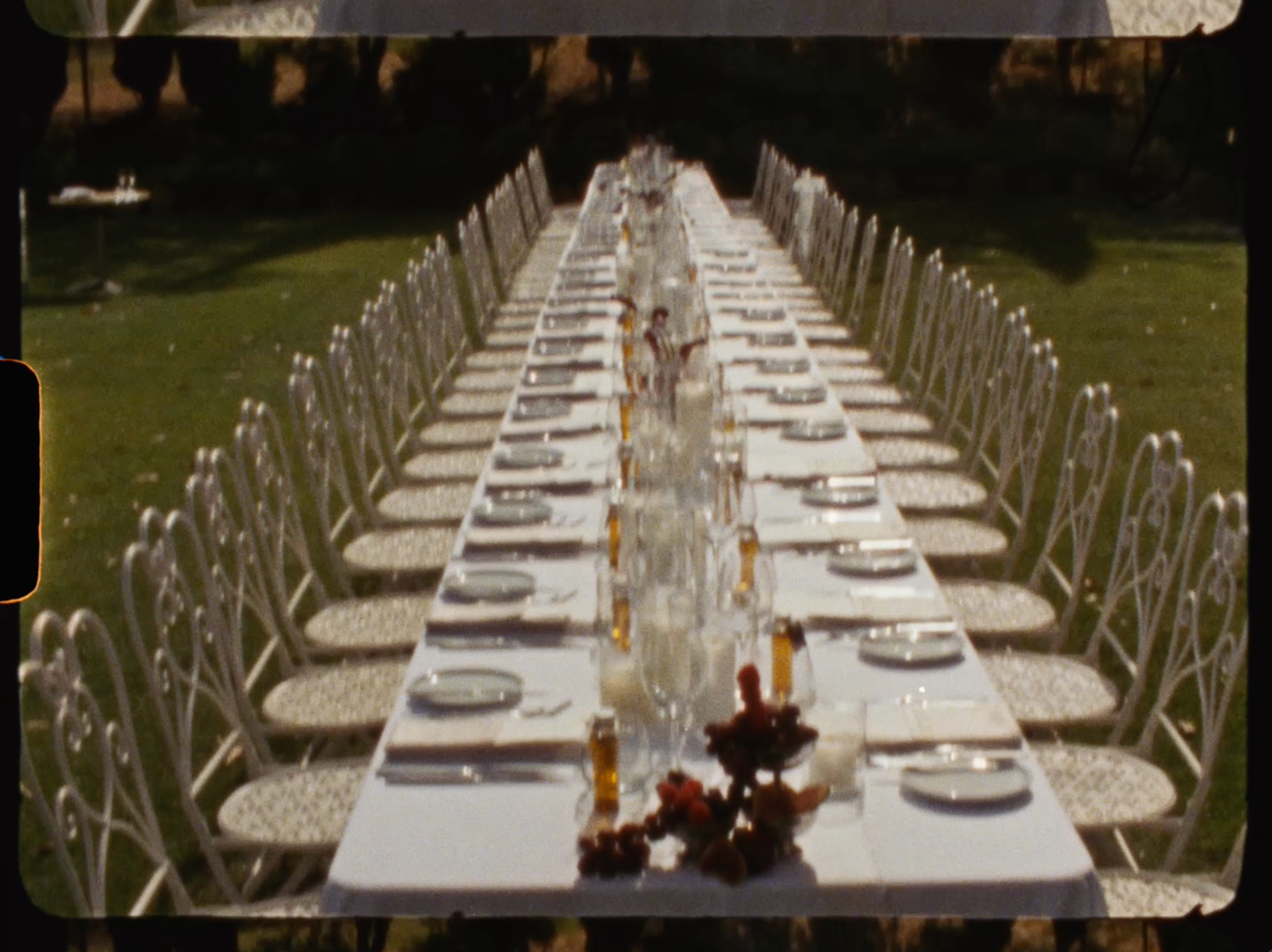 Aerial view of long outdoor wedding reception table with white linens, candles, and floral centerpieces.
