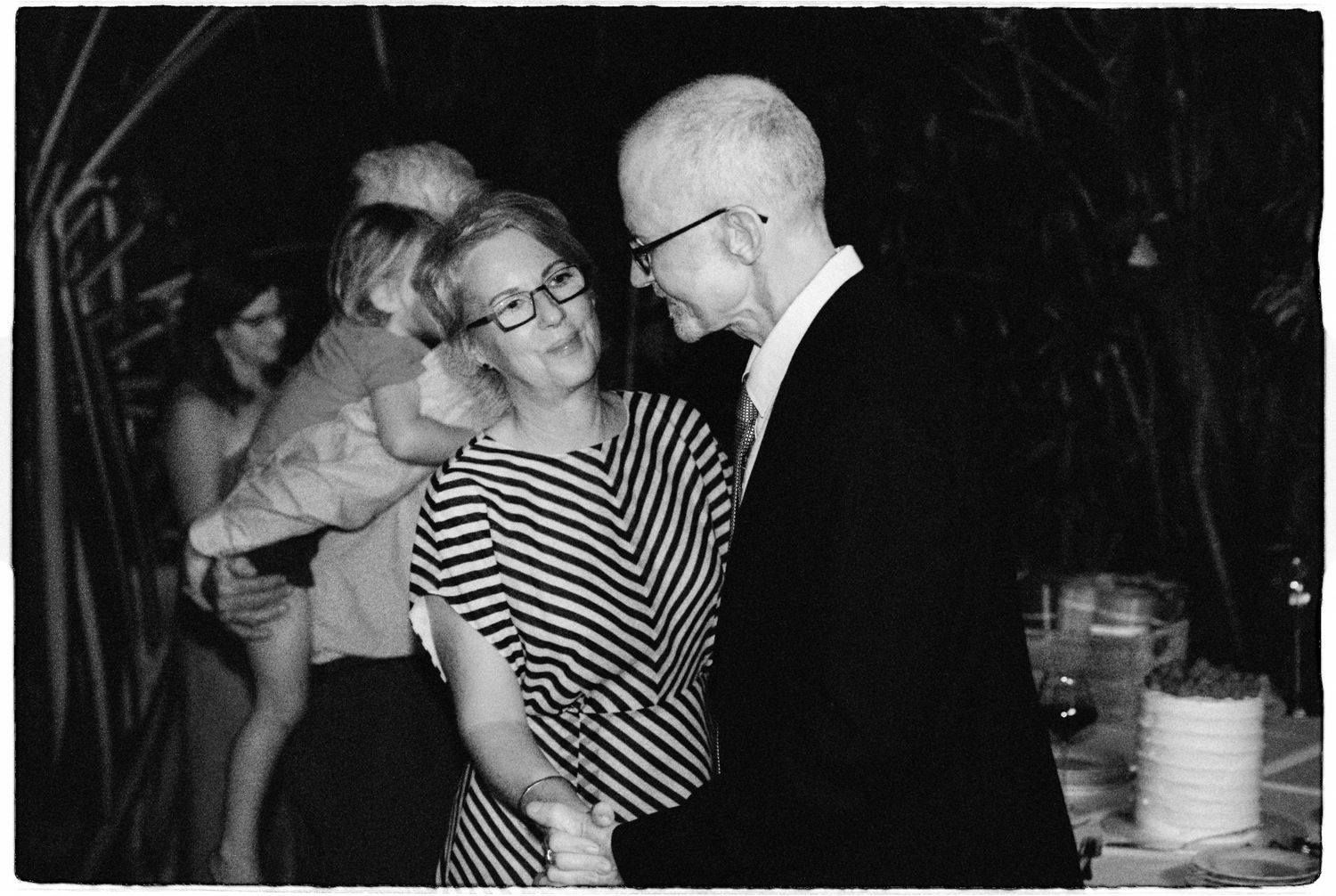 Black and white photo of wedding guests dancing and socializing at an outdoor evening wedding reception.