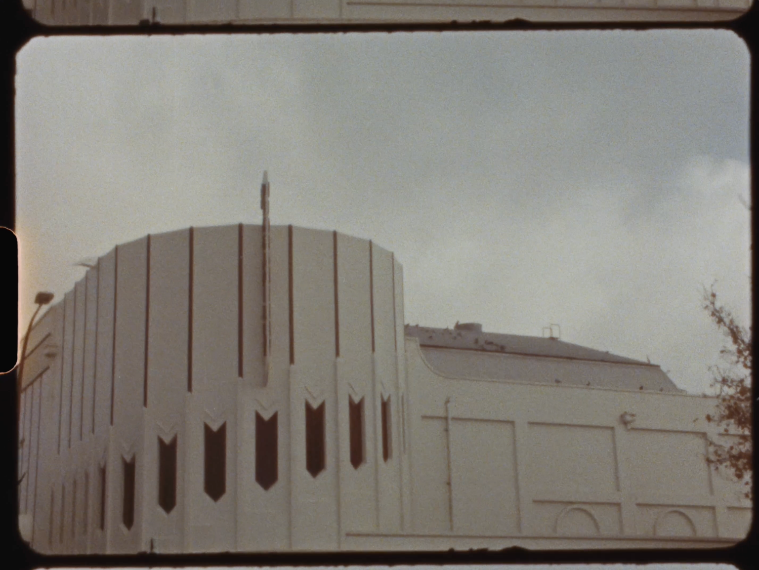 A modern white cylindrical building with decorative vertical windows under a cloudy sky.