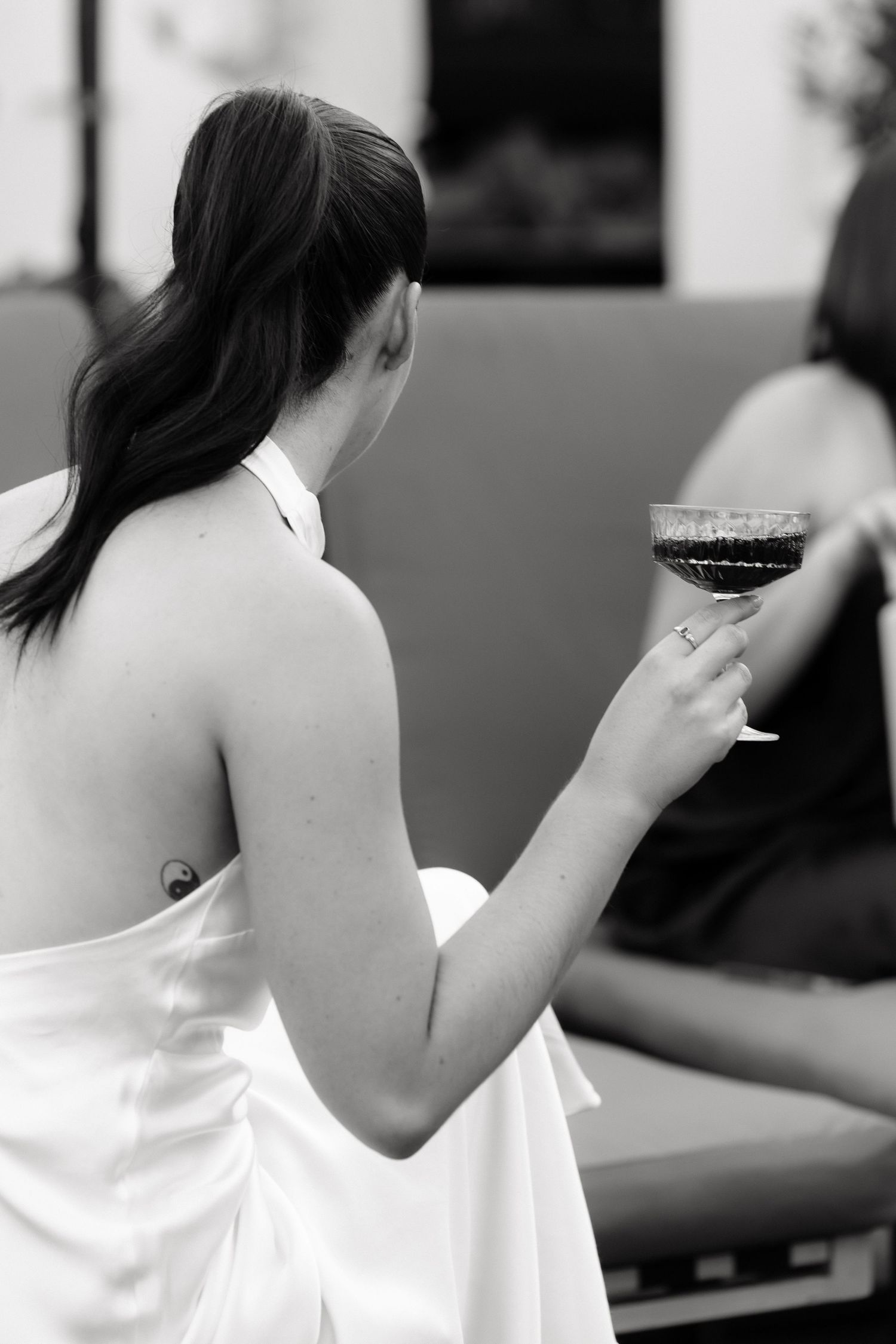 Black and white photo of a bride in white halter dress holding a wine glass at a wedding reception.