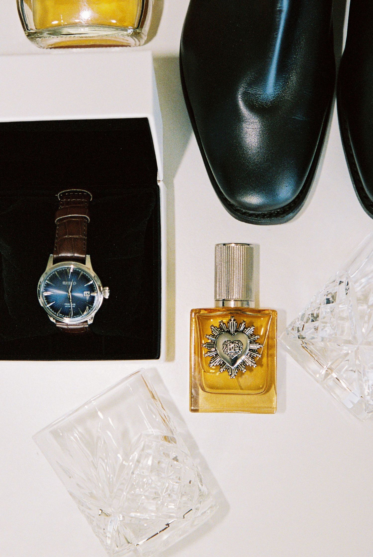 Mens wedding accessories flatlay featuring a blue dial watch, cologne bottle, crystal glasses, and black leather dress shoes.