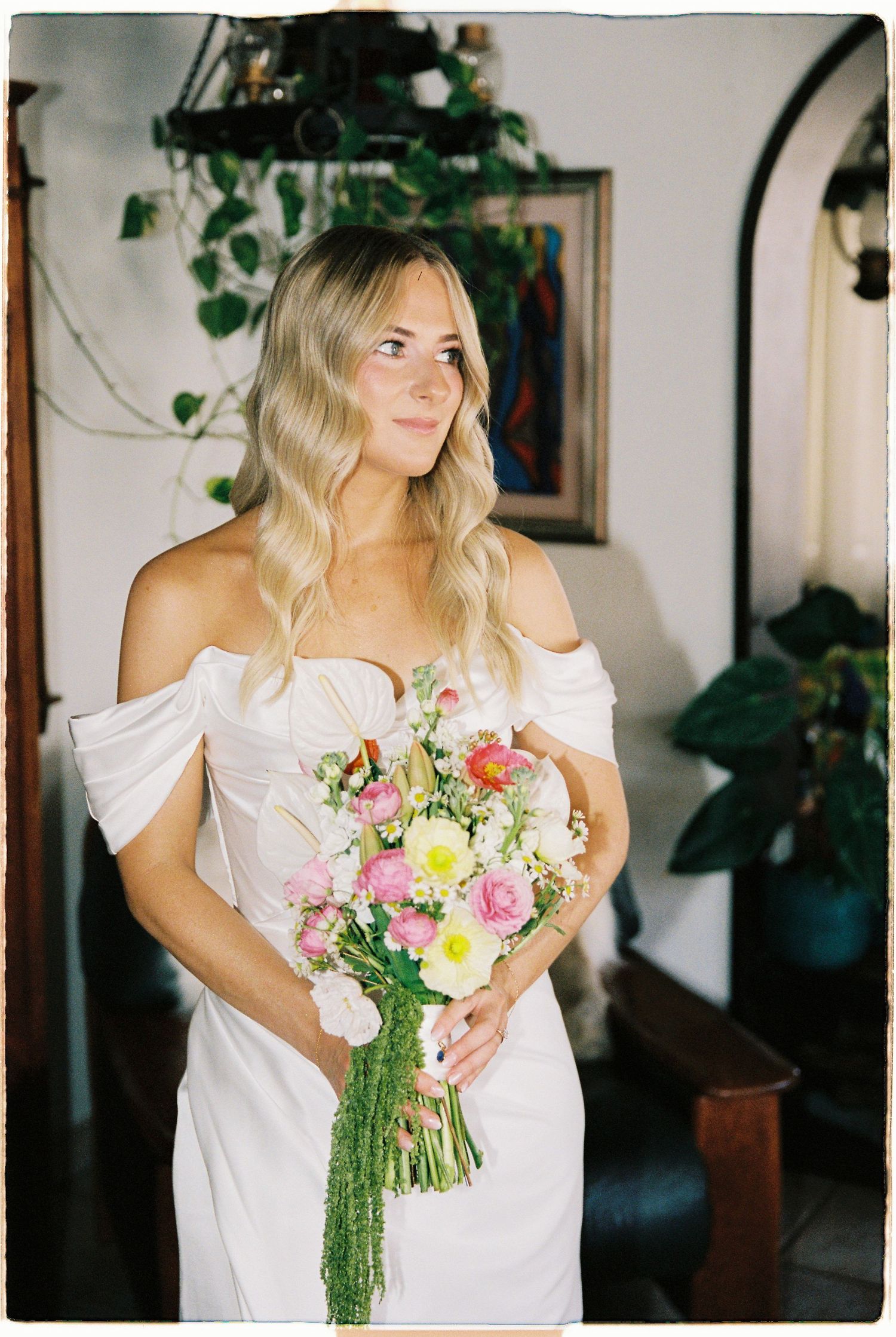 Blonde bride in off-shoulder white gown holding vibrant pink and white floral bouquet.