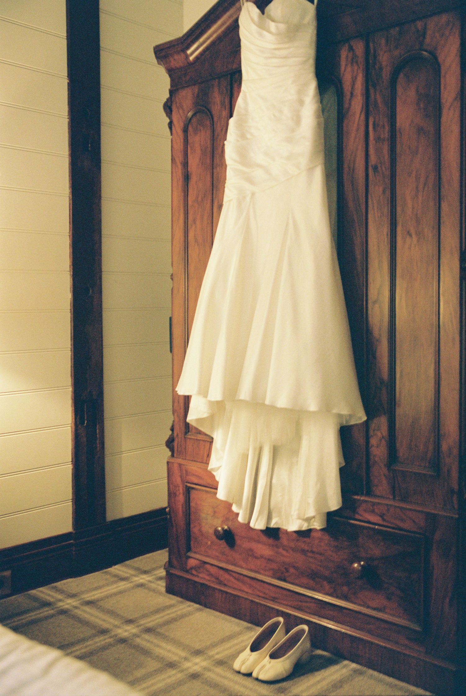 Elegant strapless white wedding gown with tiered skirt hanging on a rustic wooden armoire.