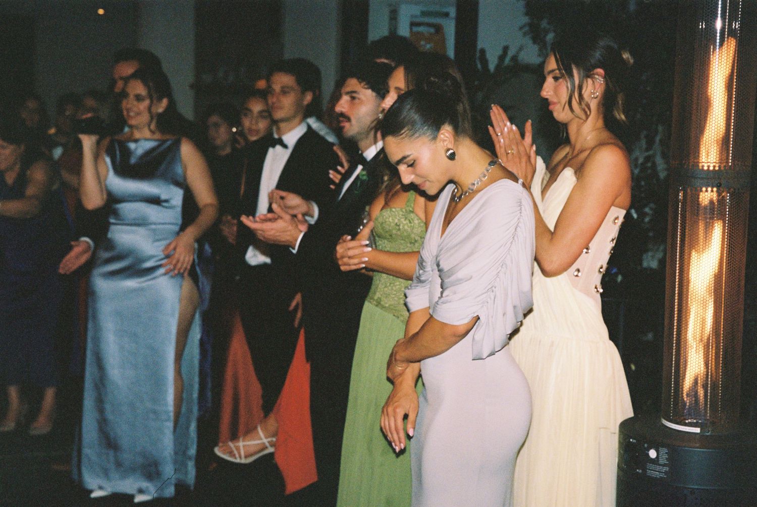 Elegantly dressed guests dancing at a formal event, wearing evening gowns in blue, green, and white.