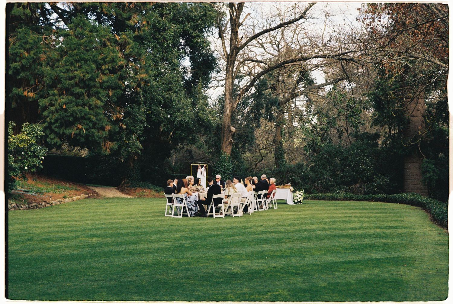 Small intimate outdoor wedding ceremony on a manicured lawn surrounded by lush trees.