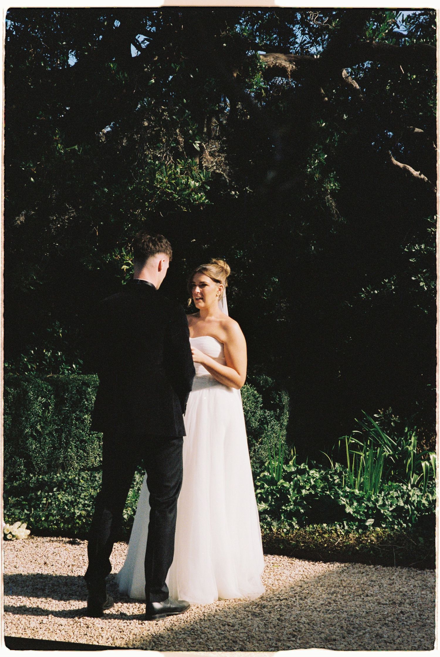 Bride and groom share an intimate first look moment in a lush garden with dark green foliage.