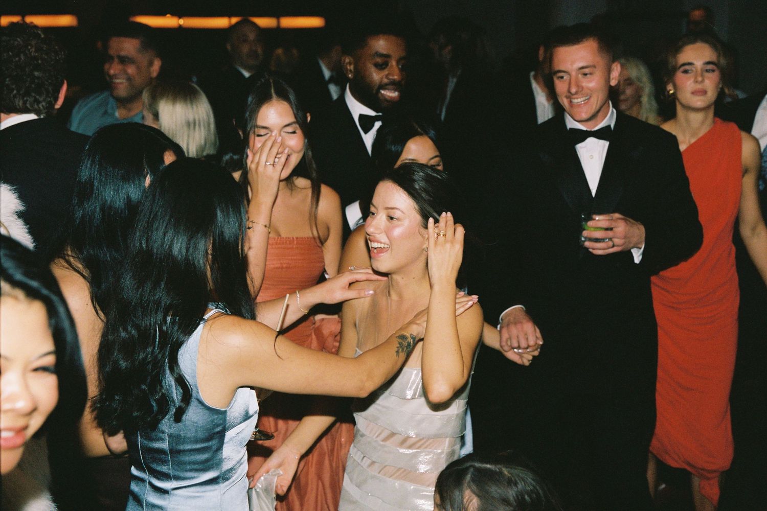 Wedding guests in elegant attire laugh and celebrate together on the dance floor.