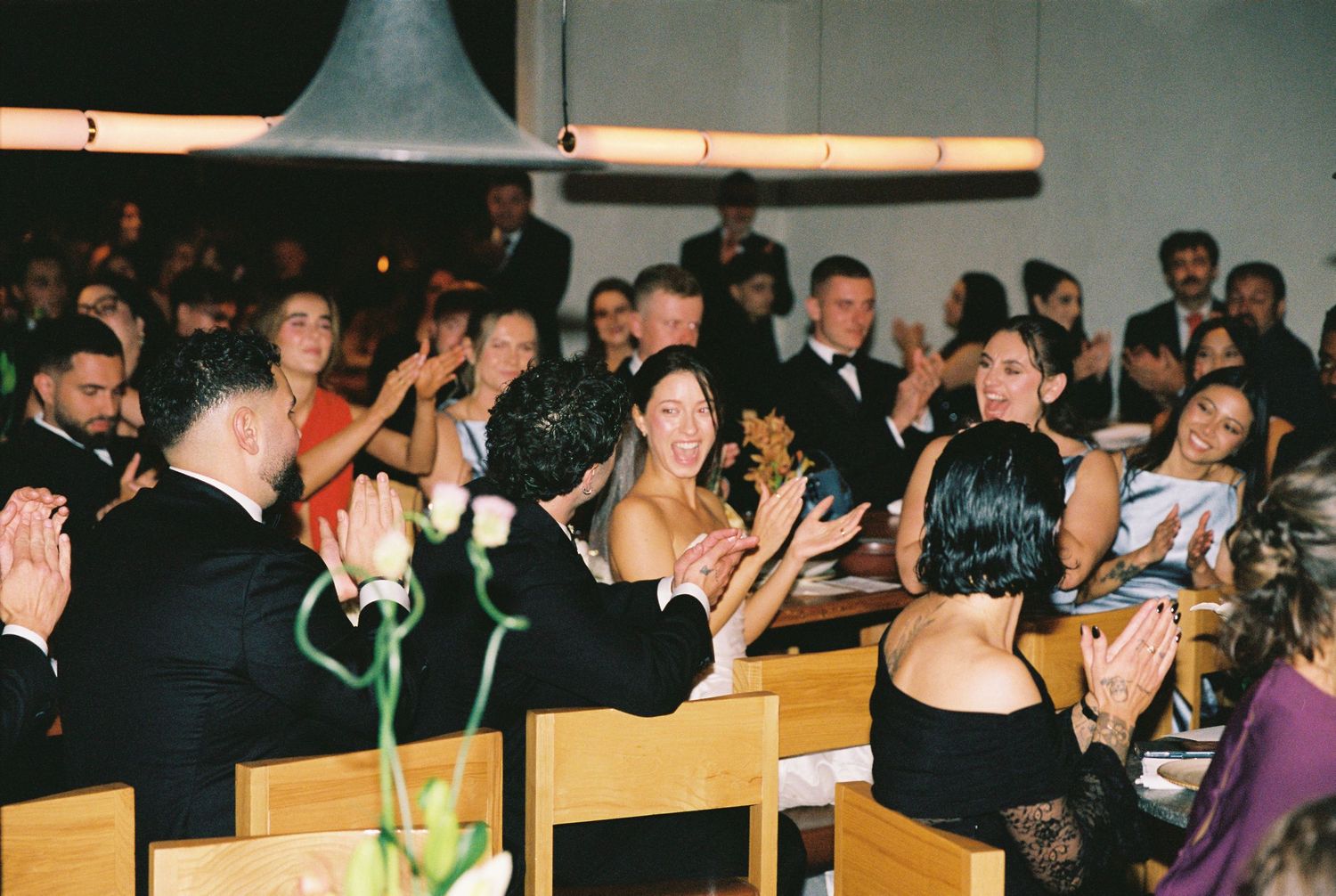 Elegantly dressed wedding guests clapping and celebrating at a formal reception dinner.