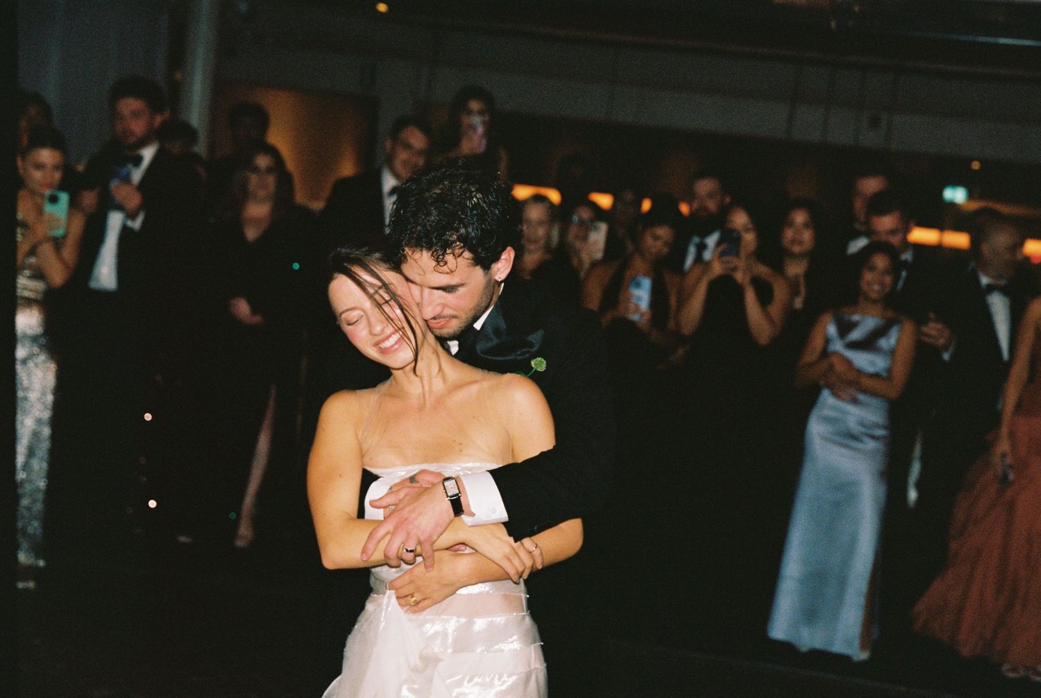 Bride and groom share an intimate first dance embrace surrounded by wedding guests.