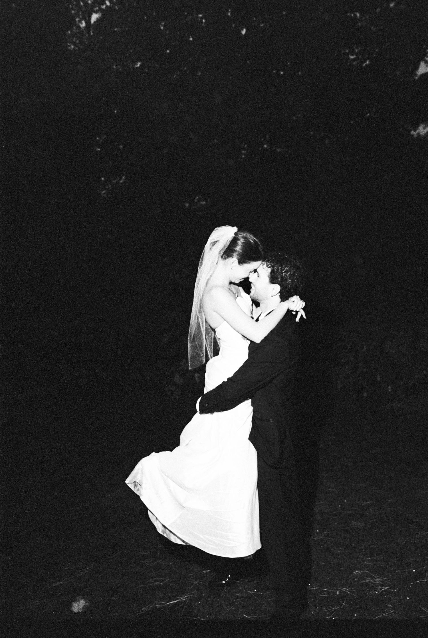 Bride and groom embrace romantically outdoors at night in a stunning black and white wedding portrait.