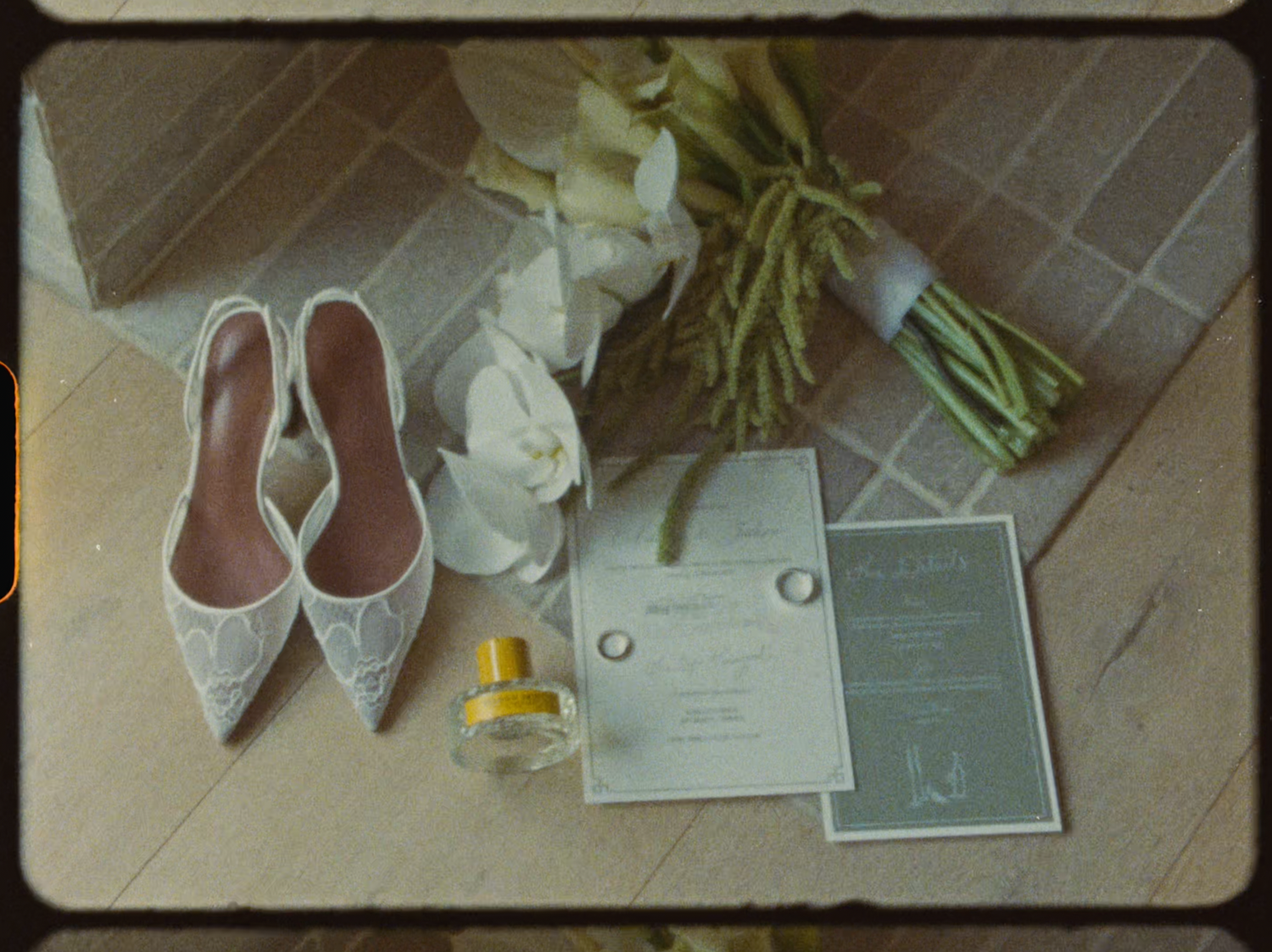 Wedding flat lay featuring lace bridal shoes, white floral bouquet, rings, and invitation.