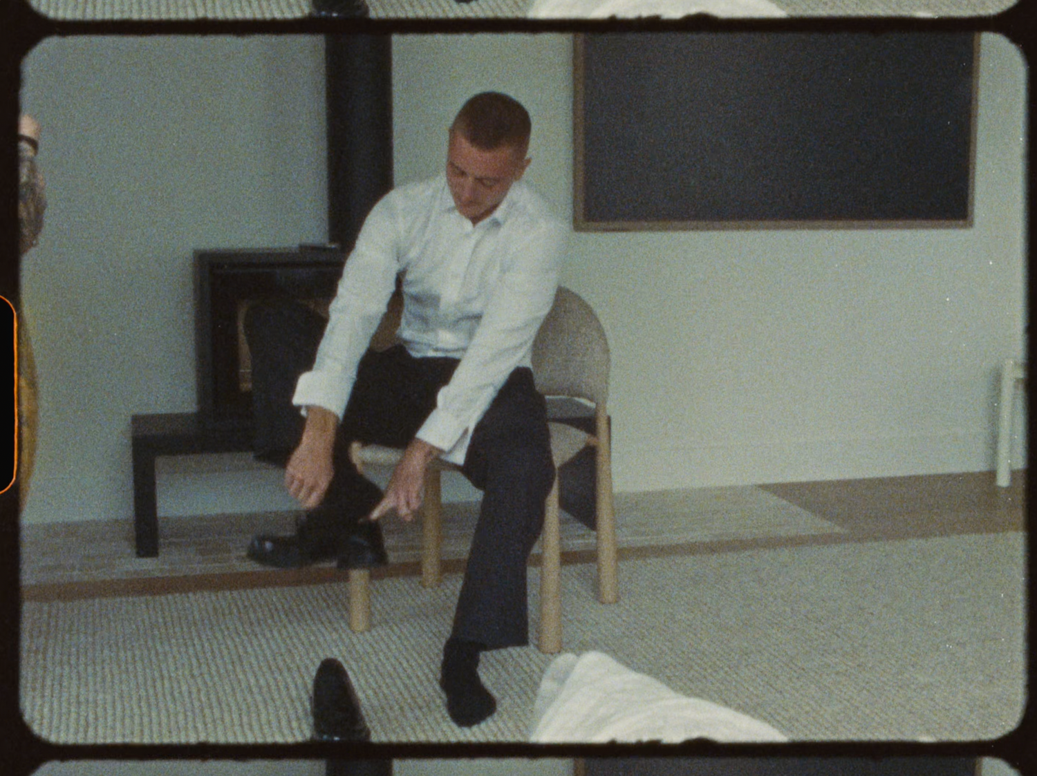 Man in white dress shirt sitting on chair putting on black dress shoes before wedding.