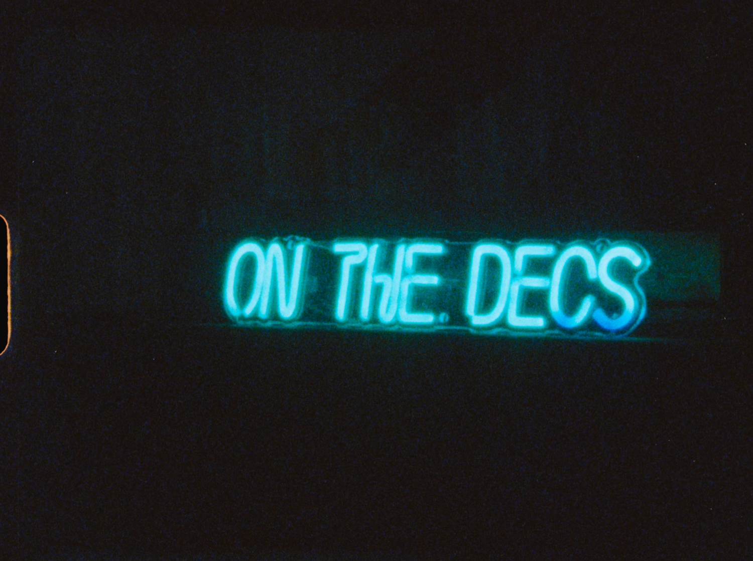 Neon blue sign reading ON THE DECS glowing in the dark at a wedding reception.