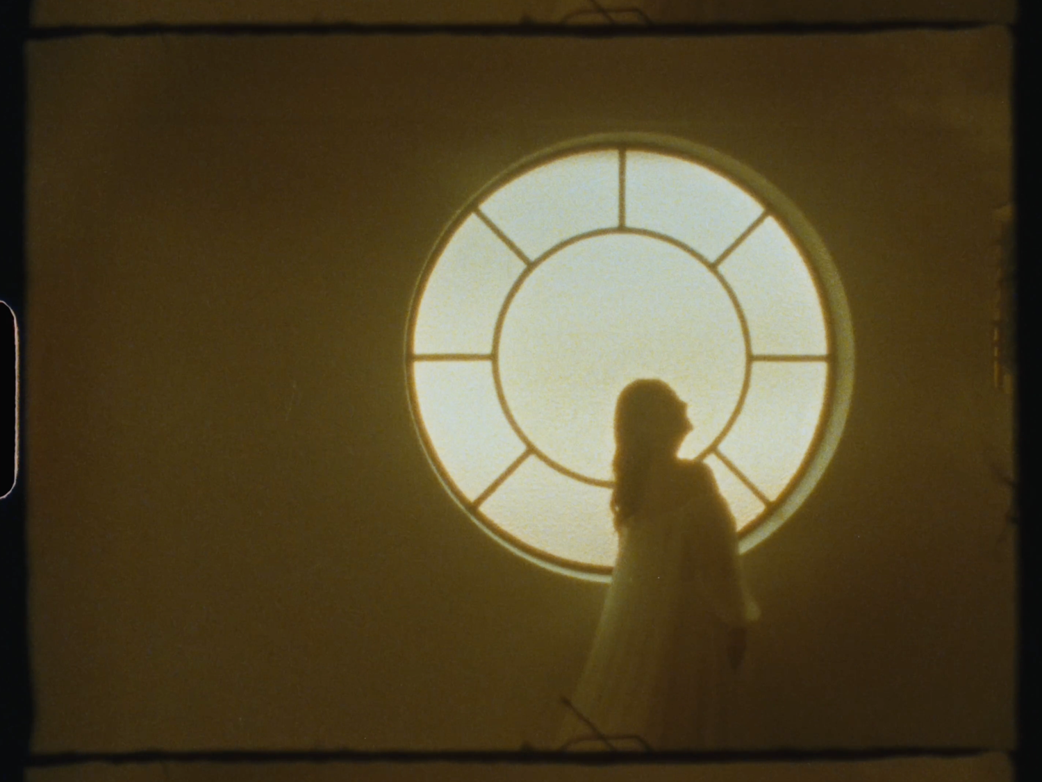 Silhouette of a bride standing before a large circular window with soft golden light.