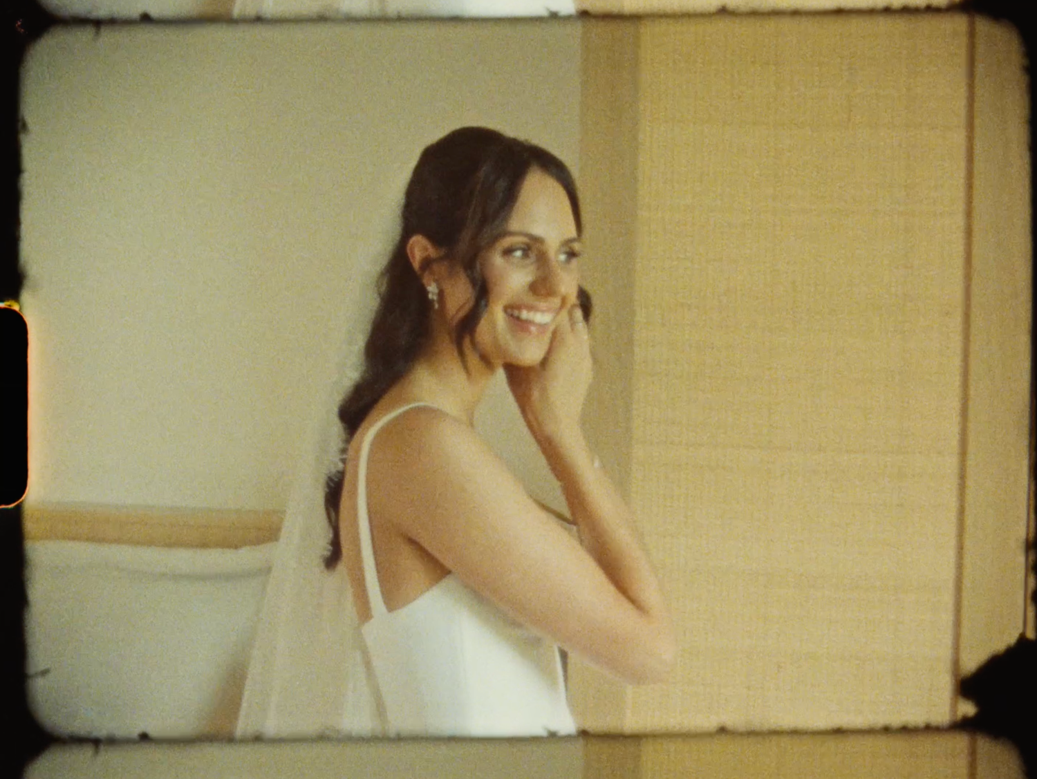Smiling brunette woman in white dress touching her face, photographed in warm vintage film style.