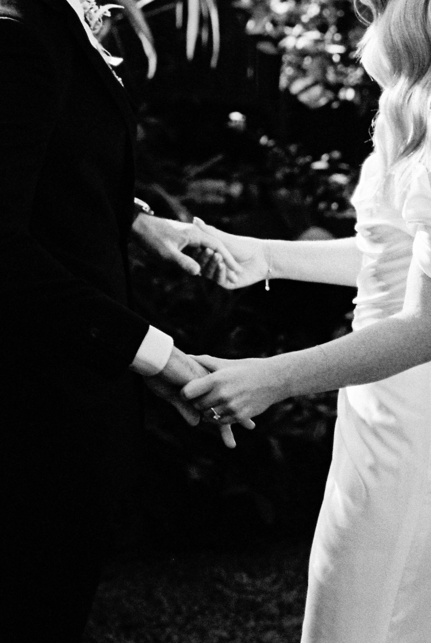 Black and white close-up of a bride and groom holding hands during their outdoor wedding ceremony.