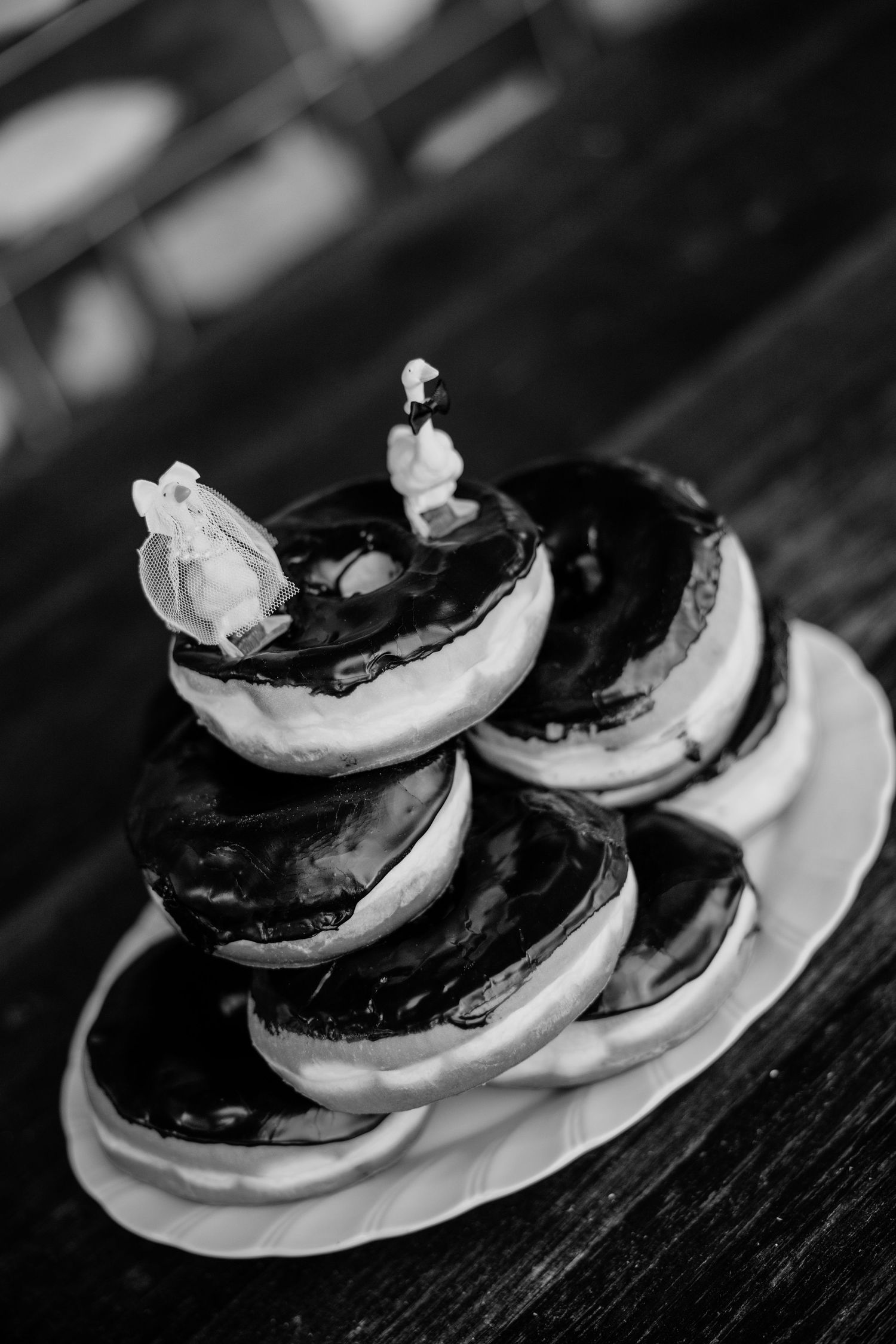 Black and white photo of a stacked donut wedding cake topped with bride and groom figurines on a white plate.