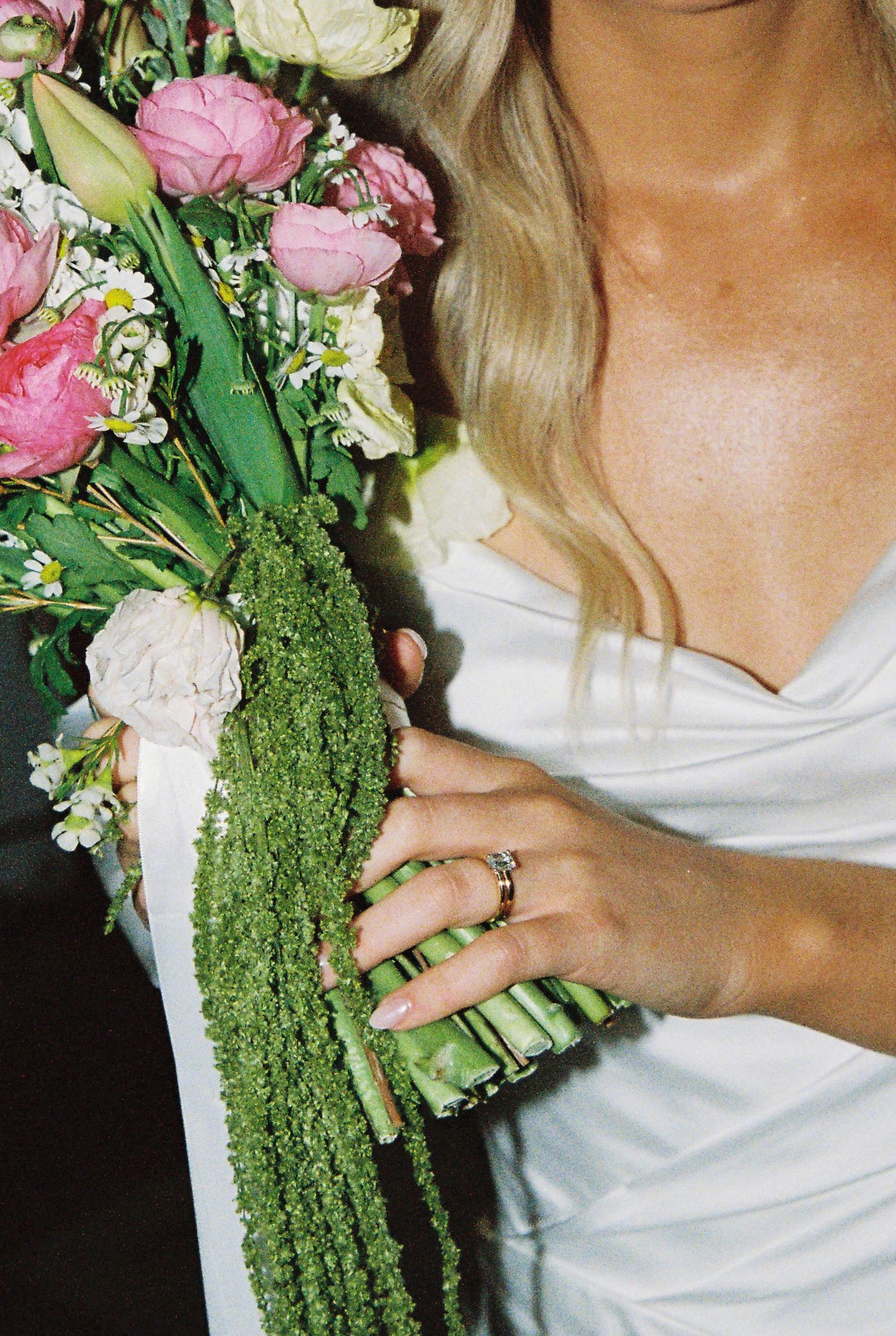 Bride holding a lush floral bouquet with pink roses and greenery, wearing a white gown and wedding ring.