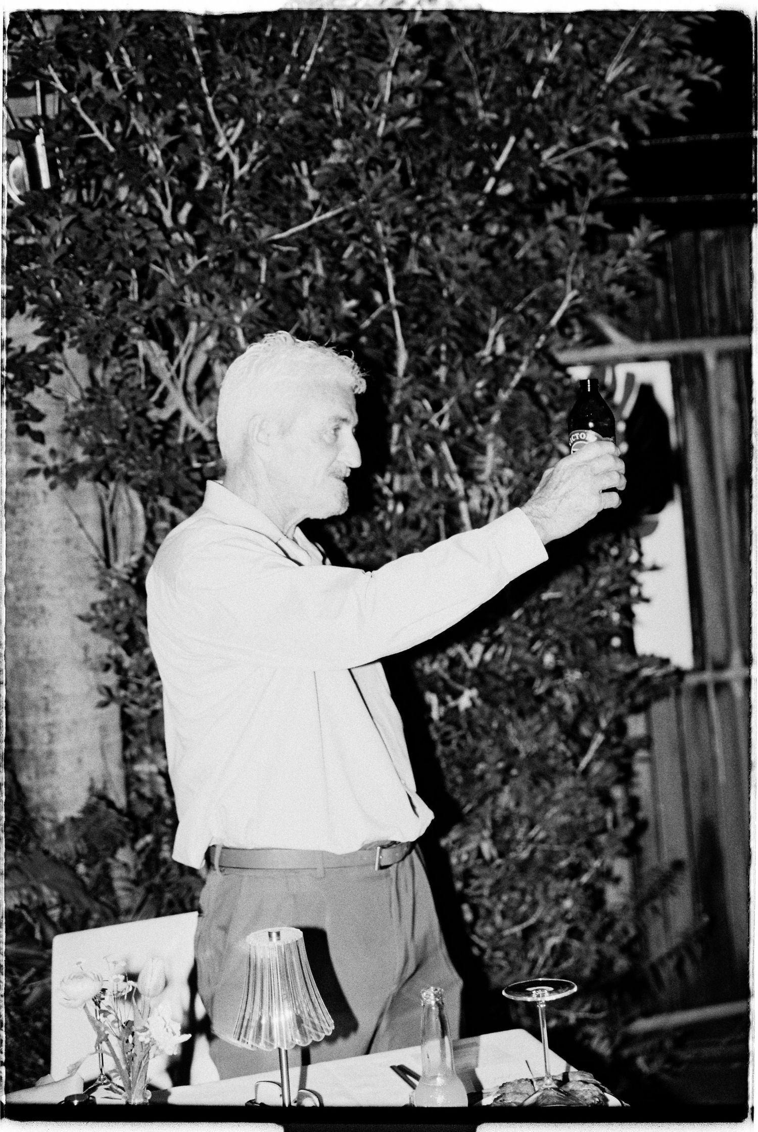 Black and white photo of man raising glass in toast at outdoor evening wedding reception.