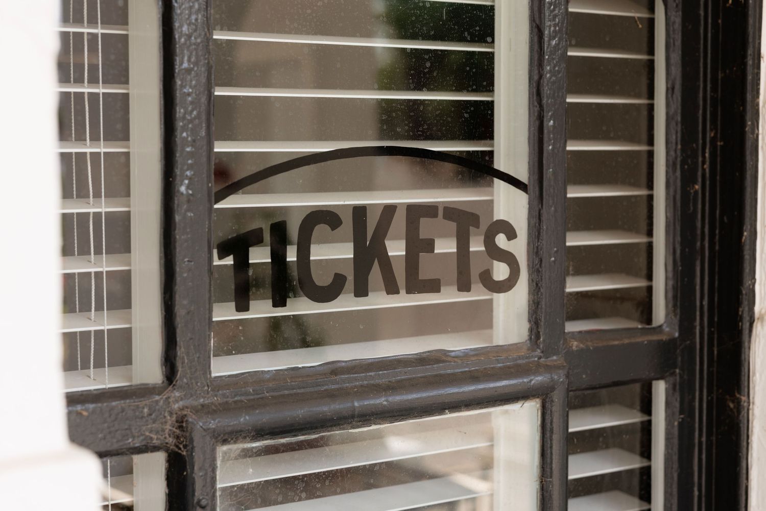 Vintage black metal tickets booth window with bold lettering on frosted glass panel.