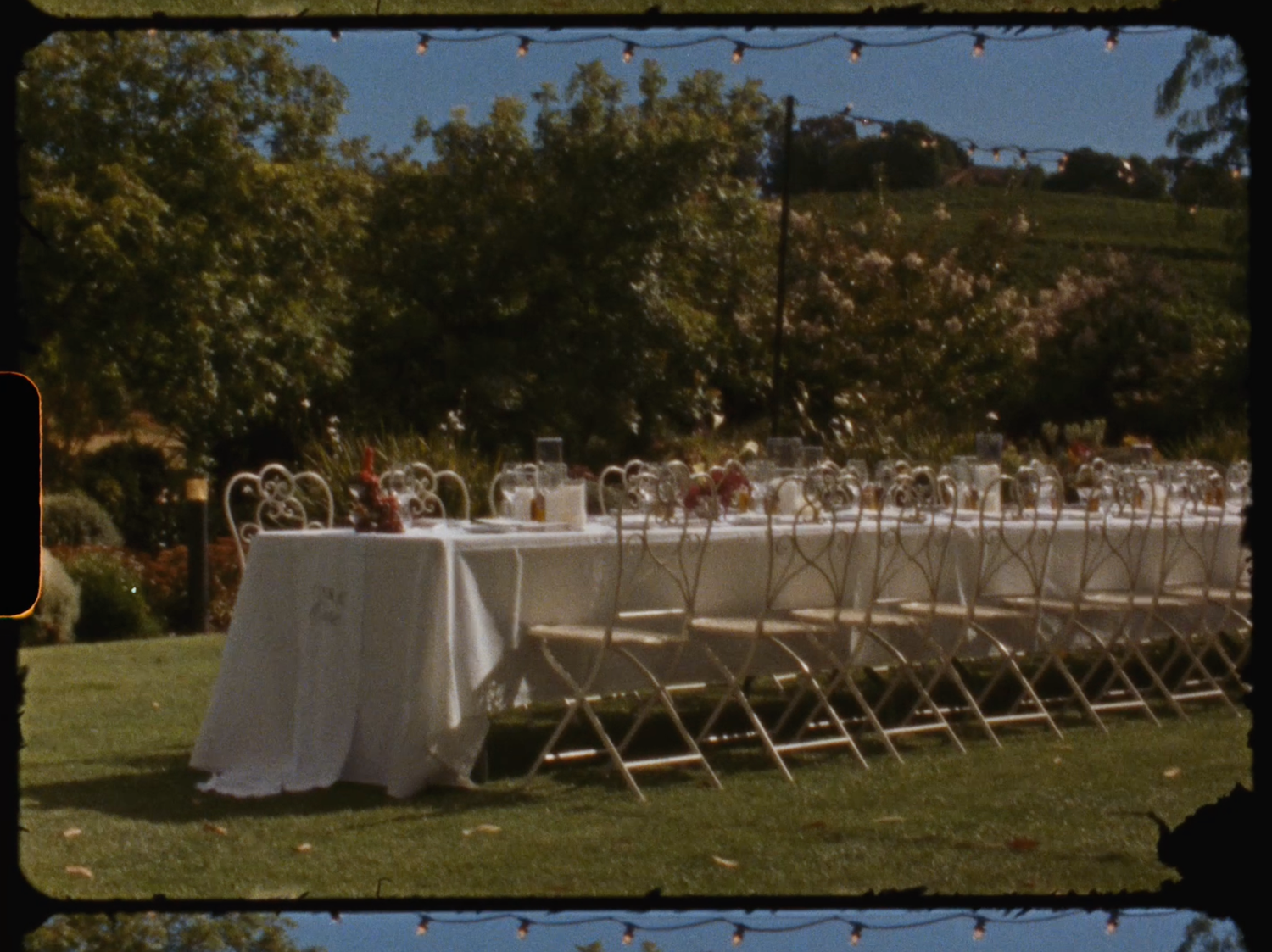 Elegant outdoor wedding reception with long table set with white linens and floral centerpieces.
