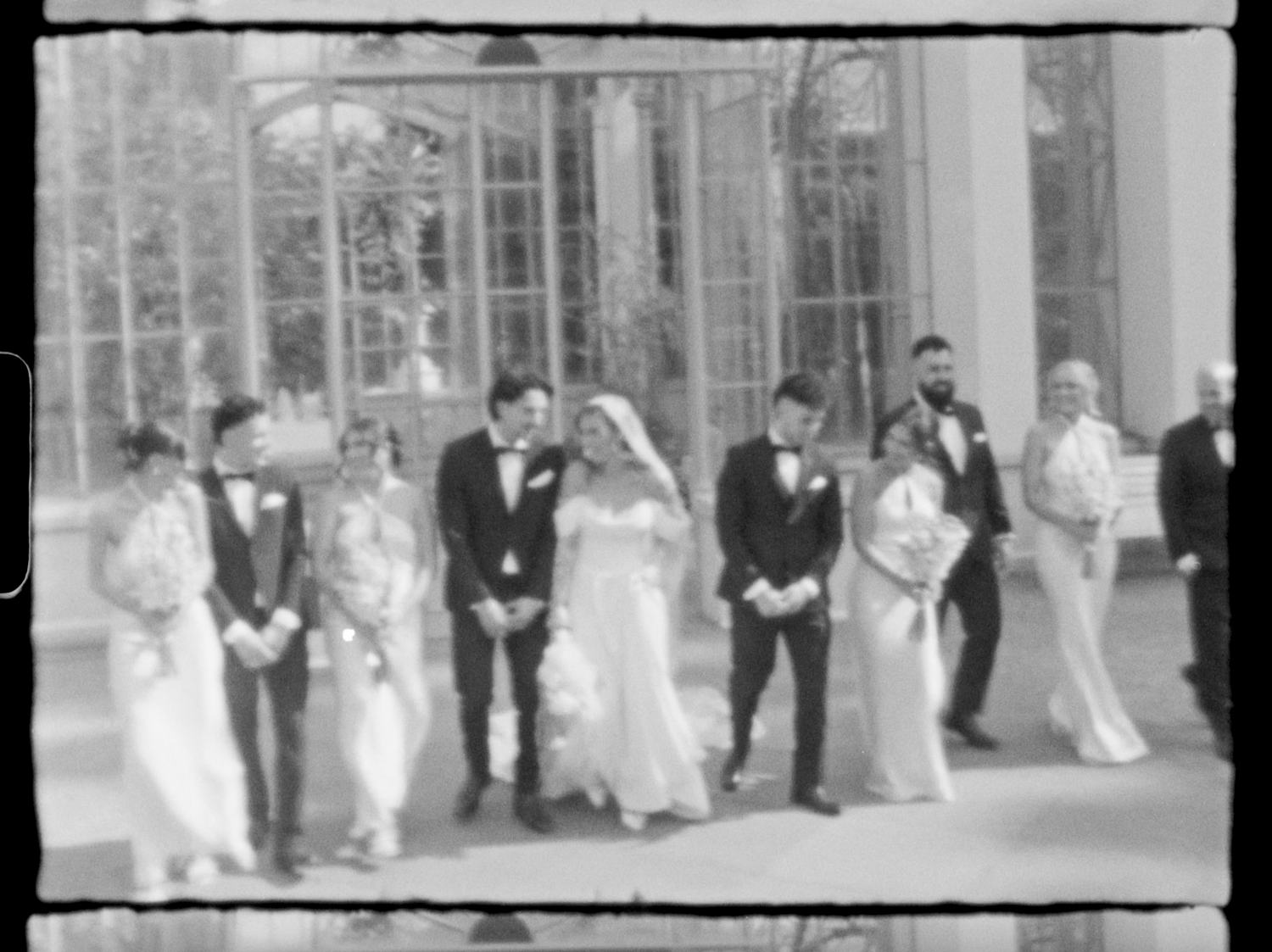 Black and white vintage wedding photo showing bride, groom, and wedding party posing outside elegant glass building.