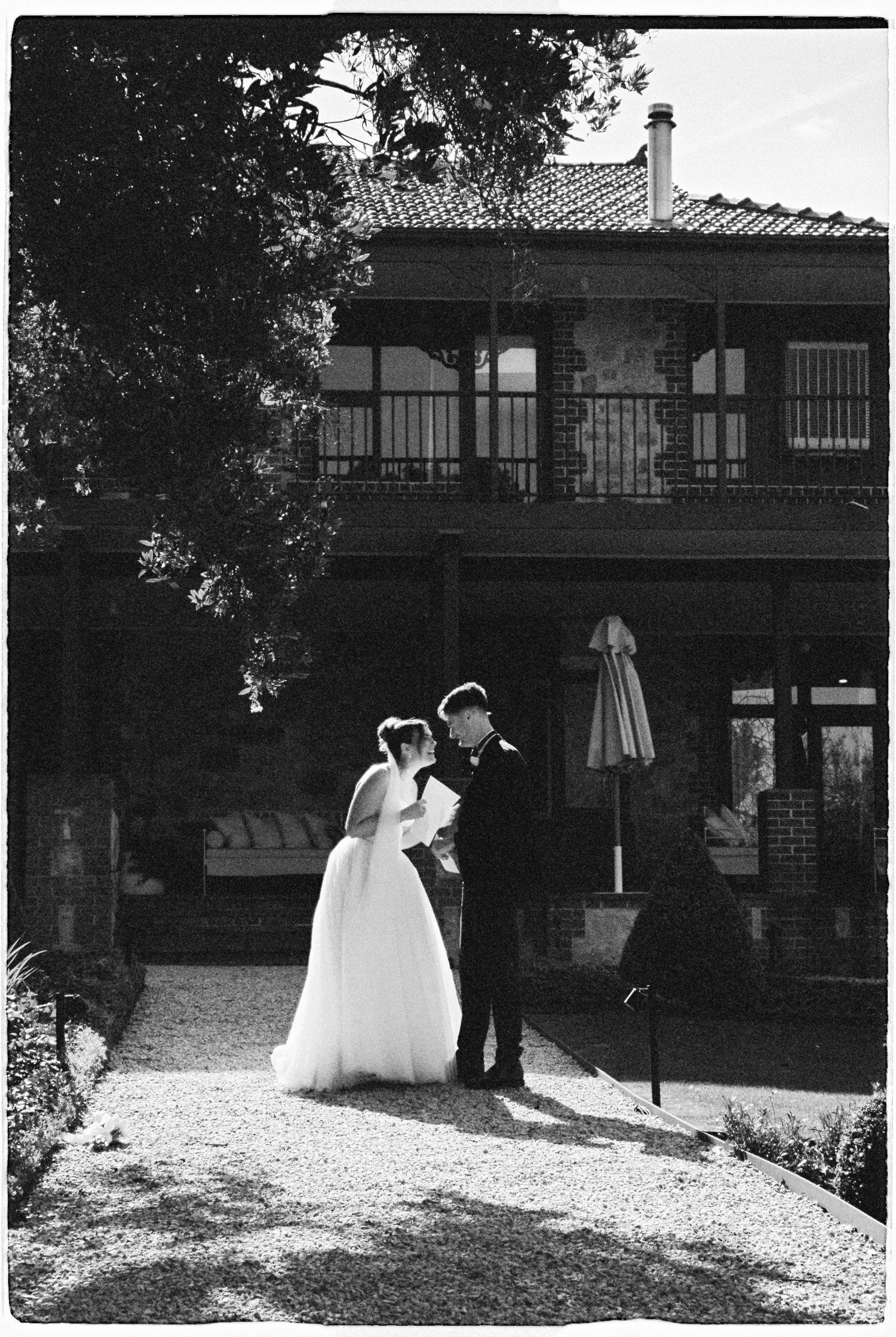 Black and white photo of a bride and groom standing together outside a historic brick building on their wedding day.