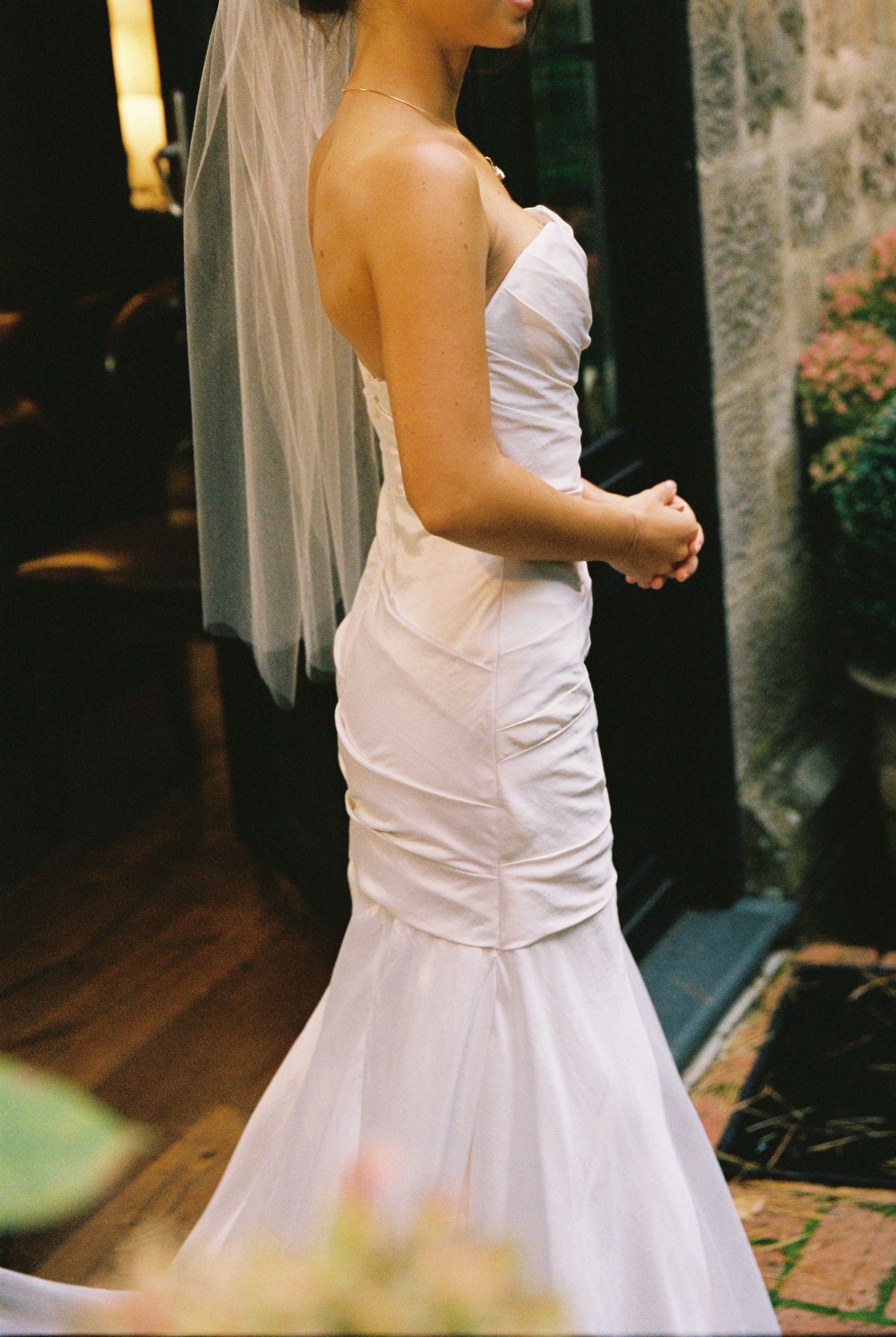 A bride in a strapless mermaid wedding gown with veil stands in a doorway.
