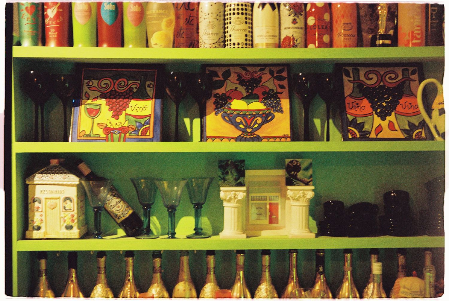 Colorful shelves displaying decorative items, green glassware, and rows of champagne bottles at wedding venue.