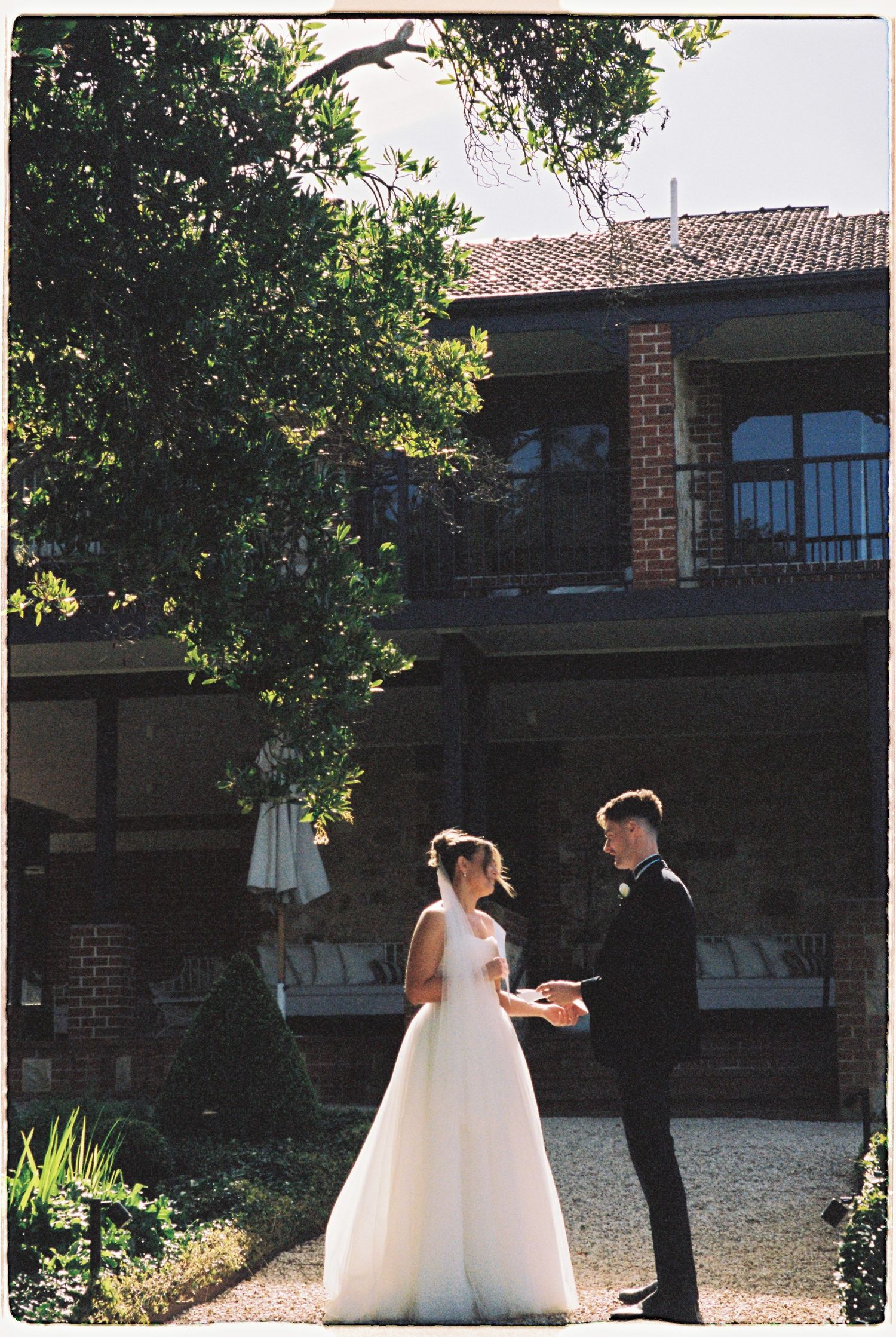 Bride and groom exchanging vows during outdoor wedding ceremony beside historic brick building.
