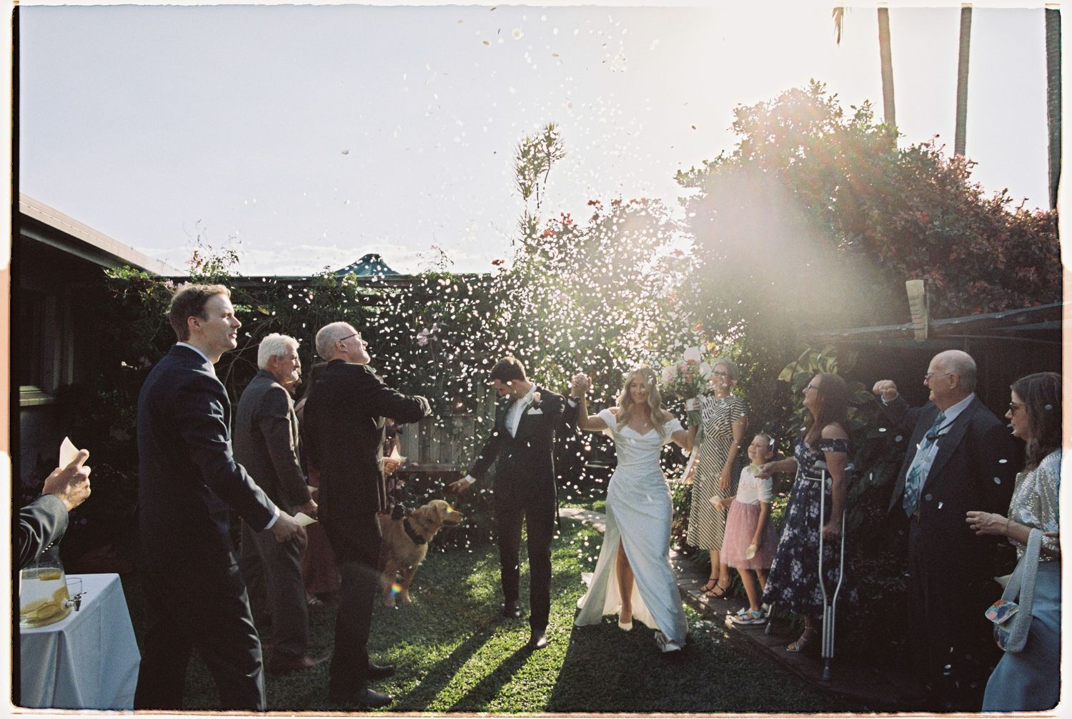 Guests shower bride and groom with confetti during joyful outdoor backyard wedding celebration.