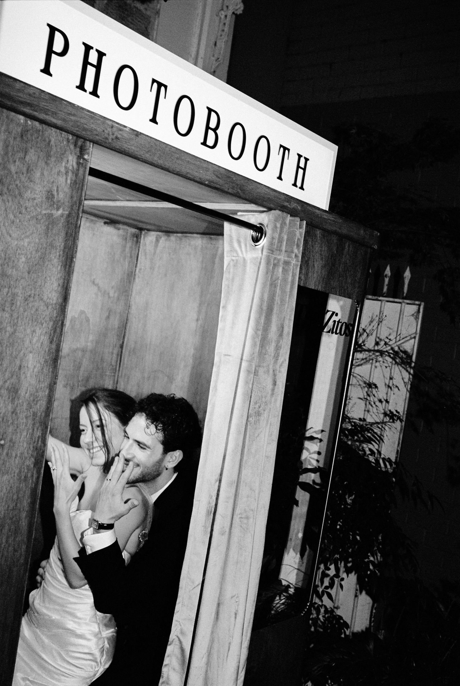 Bride and groom laughing together inside a vintage wooden photo booth at night.