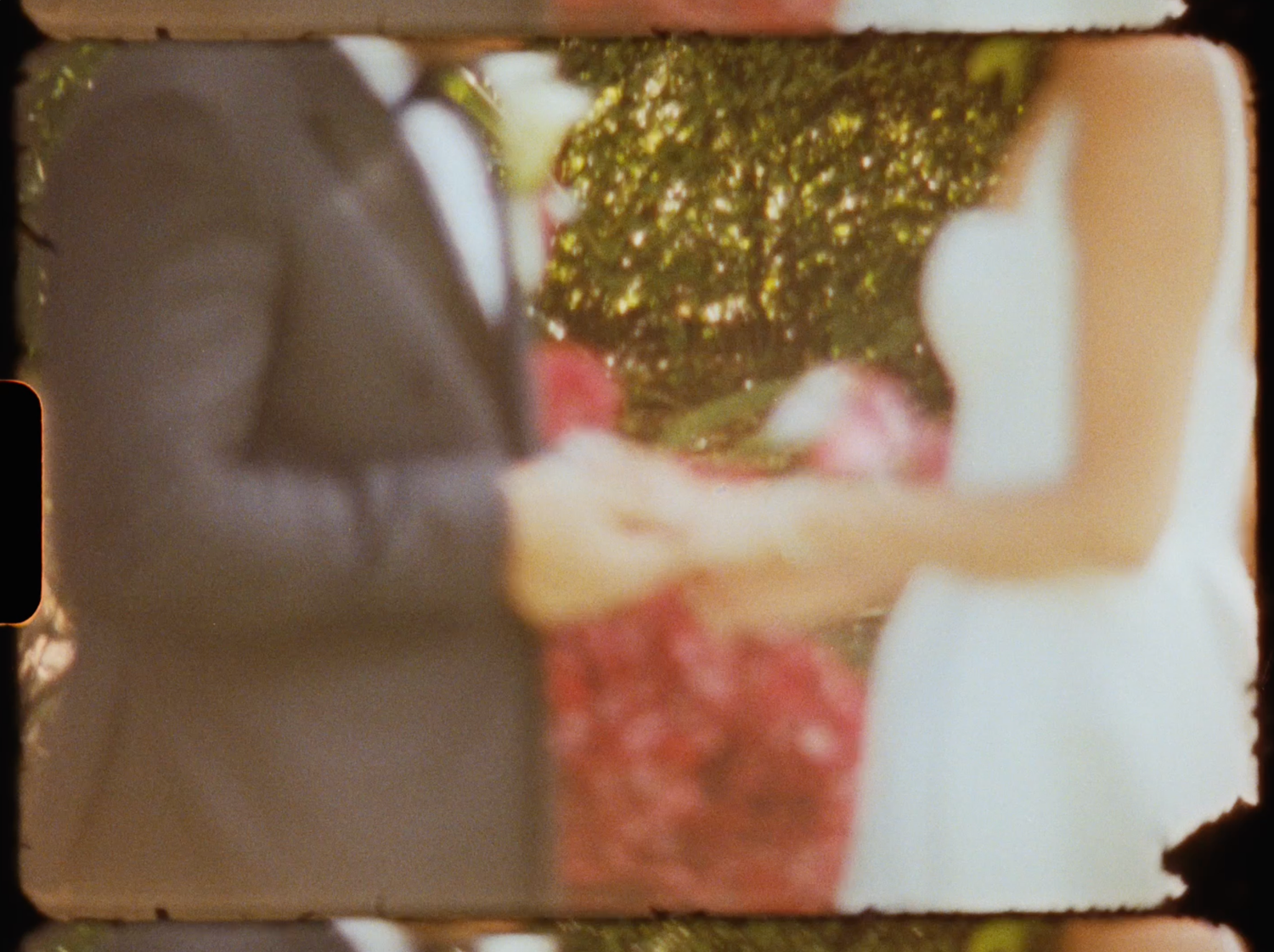 Blurred vintage film photo of bride and groom exchanging rings outdoors with red floral background.