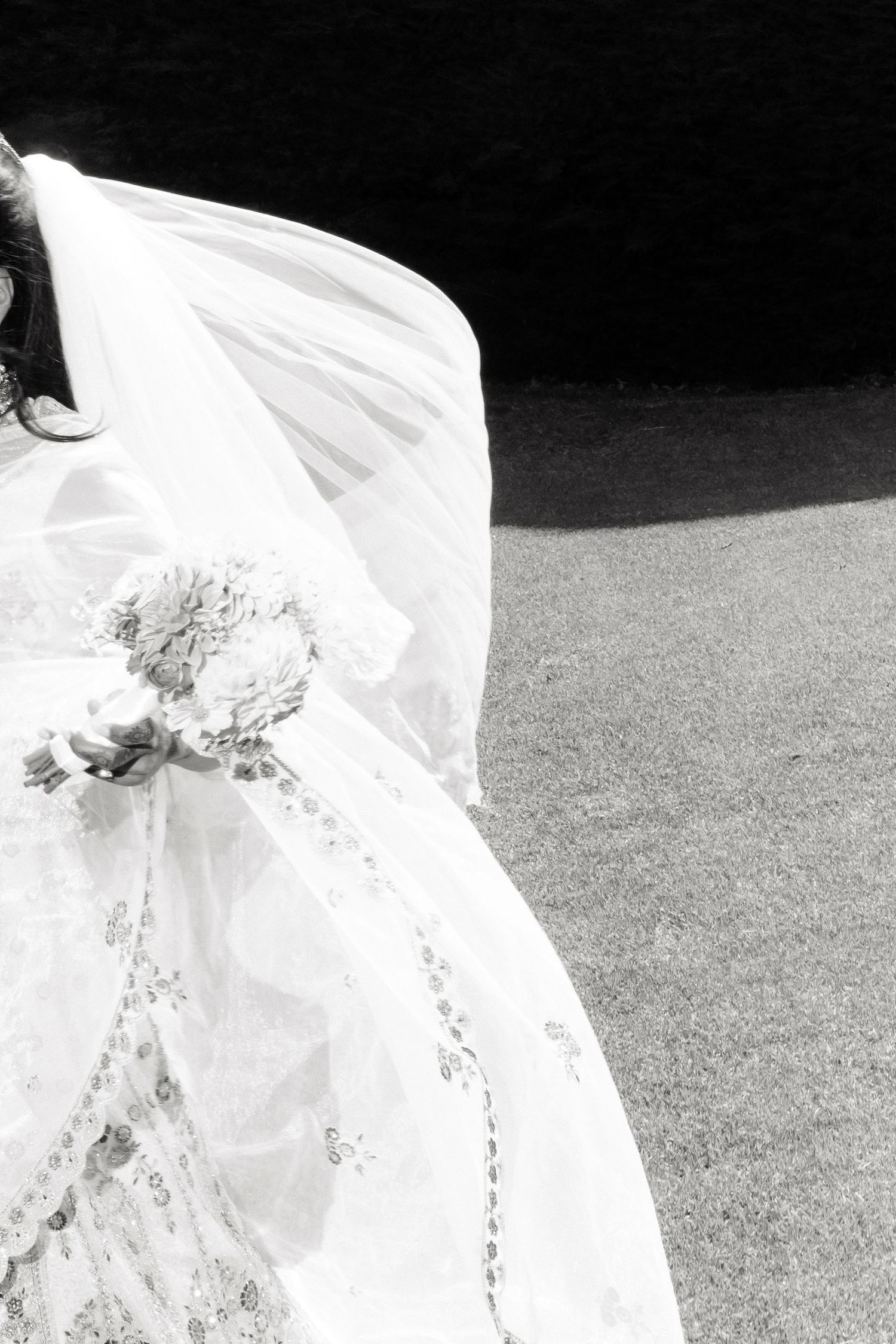 Black and white close-up of bride in white lace wedding dress holding a floral bouquet.