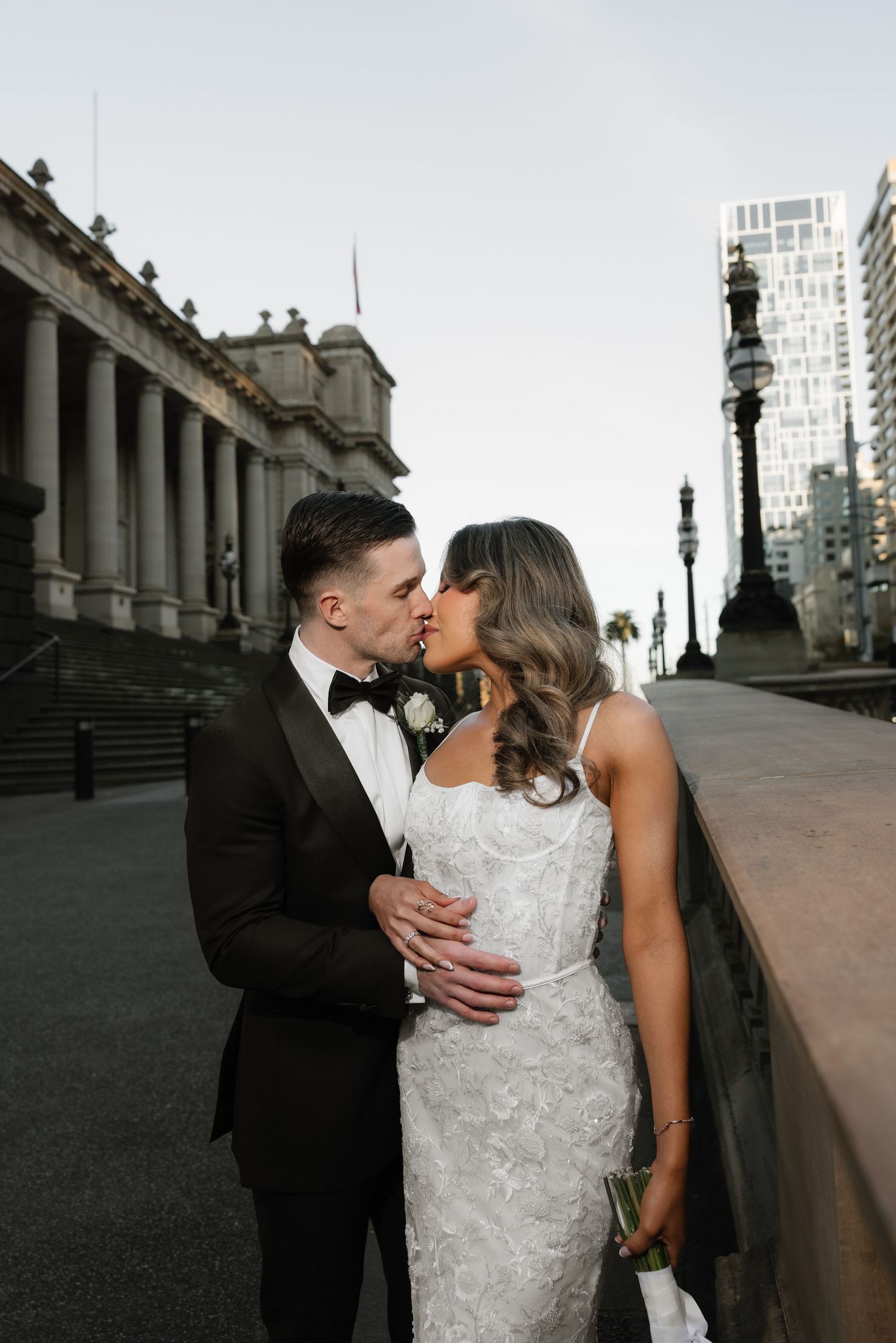 Bride and groom share a romantic kiss outside a grand classical building on their wedding day.
