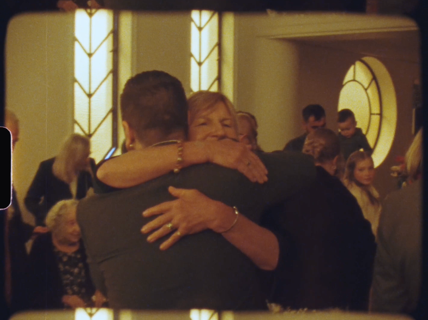Two people share a warm embrace inside a church during a wedding reception gathering.