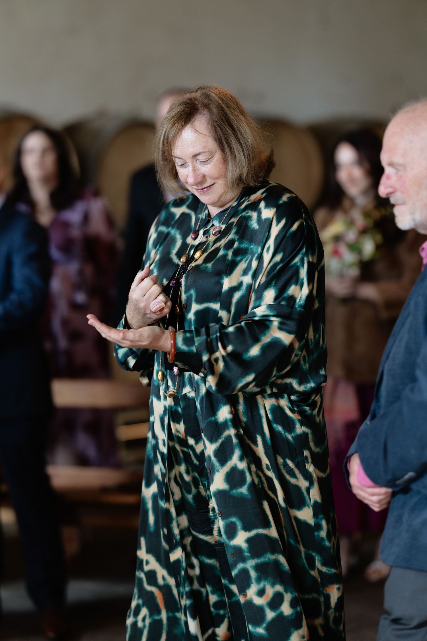 Elegant woman in green leopard print silk dress smiling at an indoor winery wedding reception.