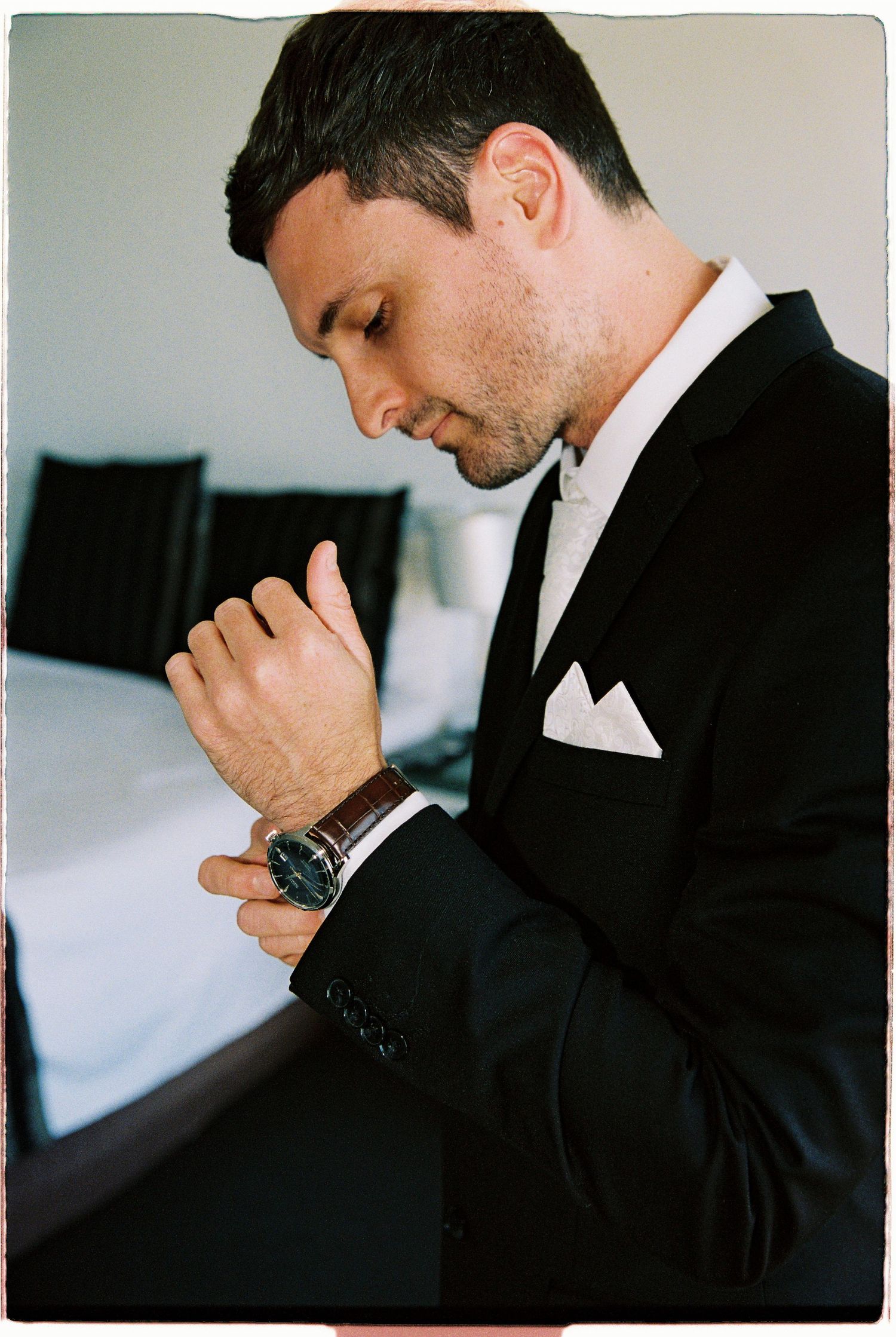 Groom in black tuxedo adjusting his watch while getting ready for his wedding day.